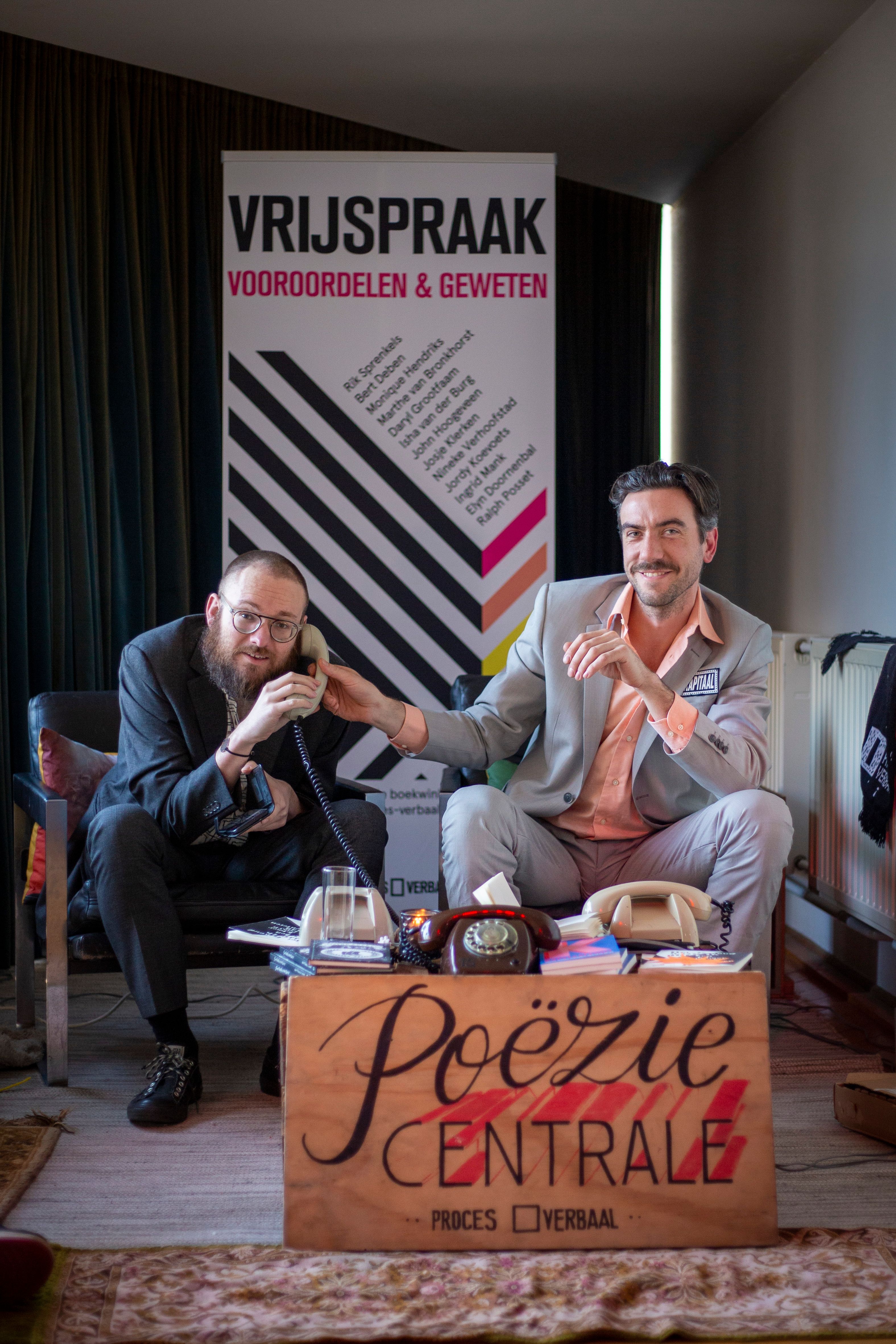 Foto van twee kunstenaars met een telefoon en een bord met daarop 'poëziecentrale'