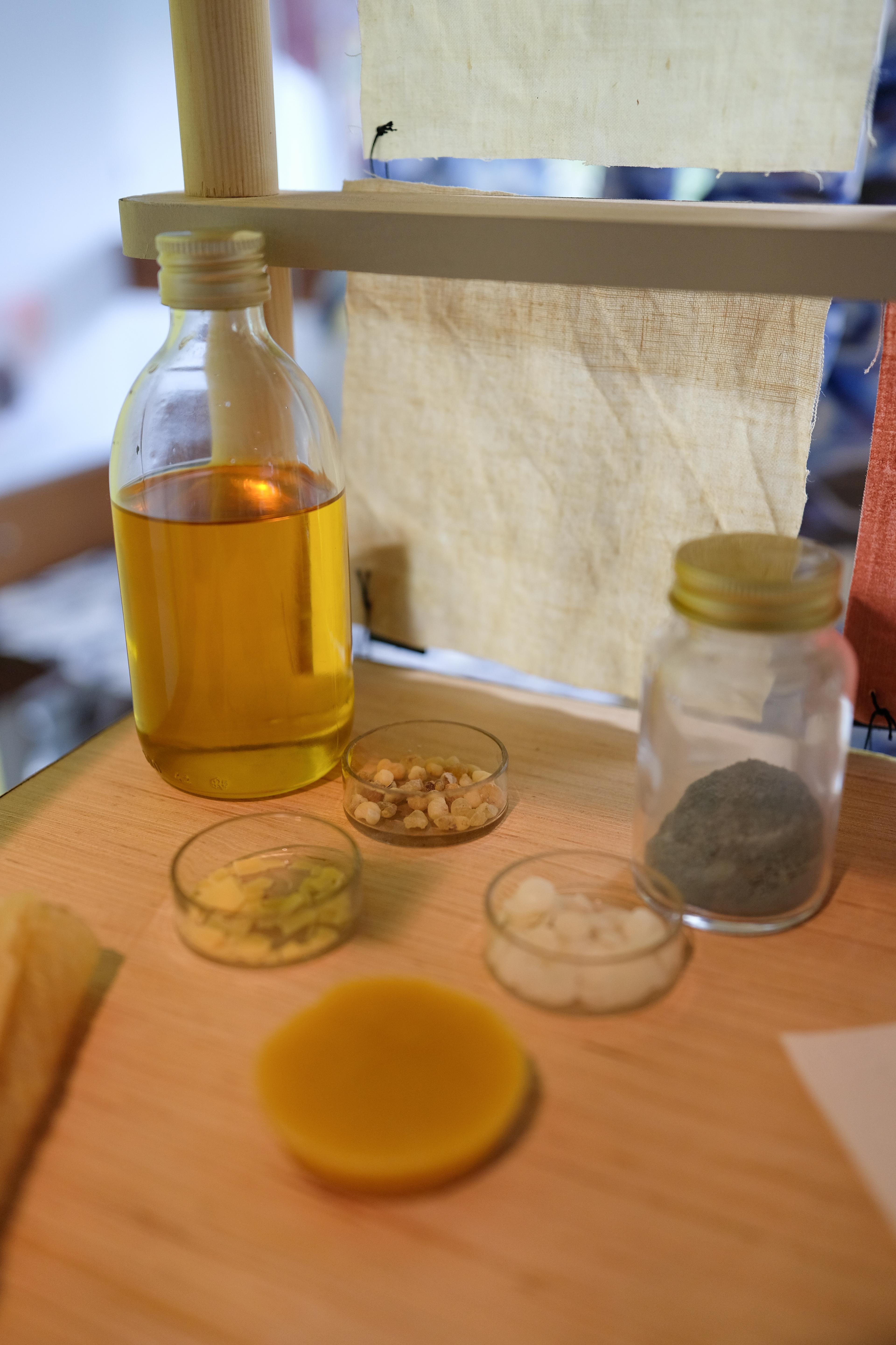 We zien een aantal glazen potjes en bakjes waarin ingredienten van de coatings waar de ontwerper mee werkte op een tafel staan.