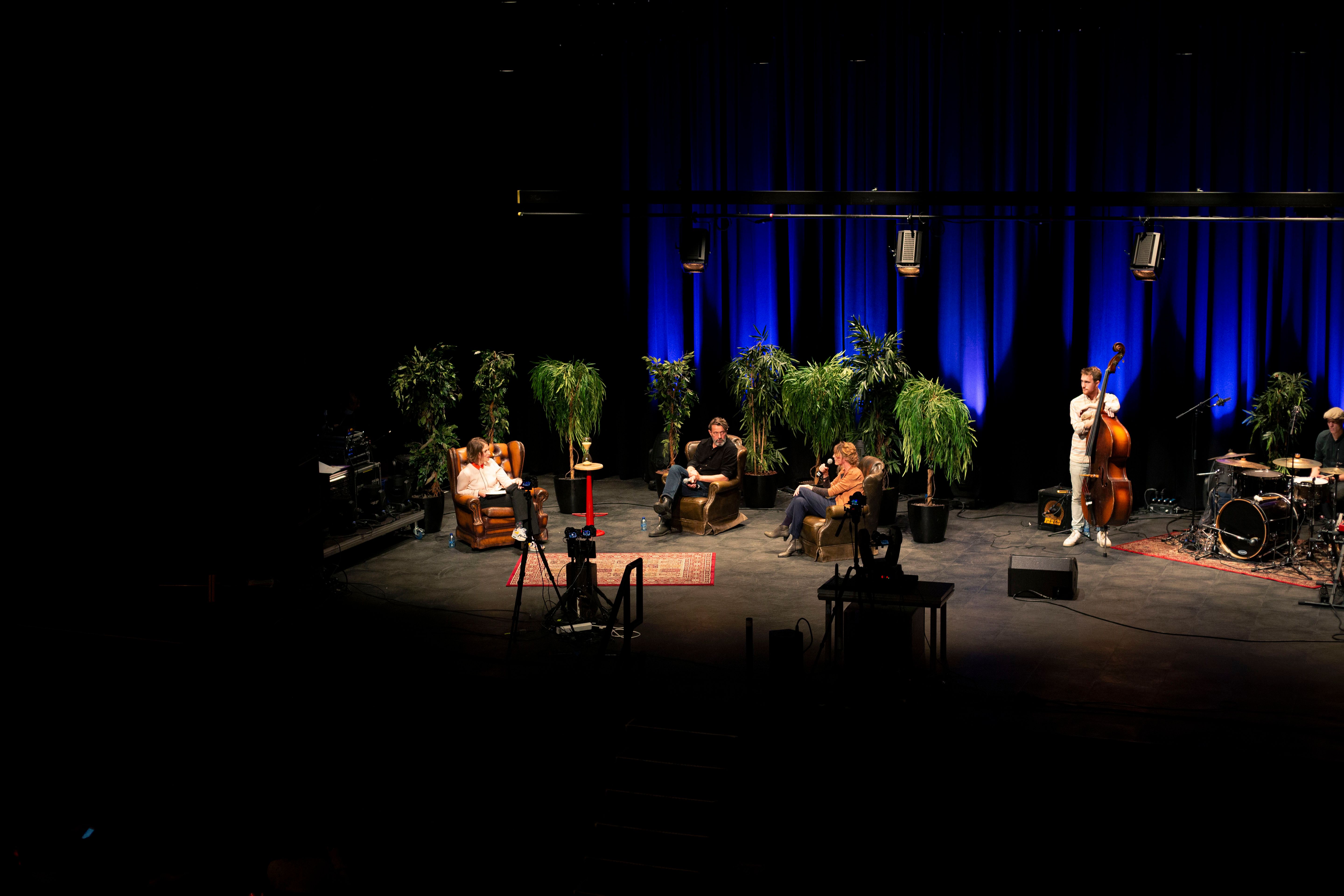 Foto van het podium, met daarop drie mensen en een band