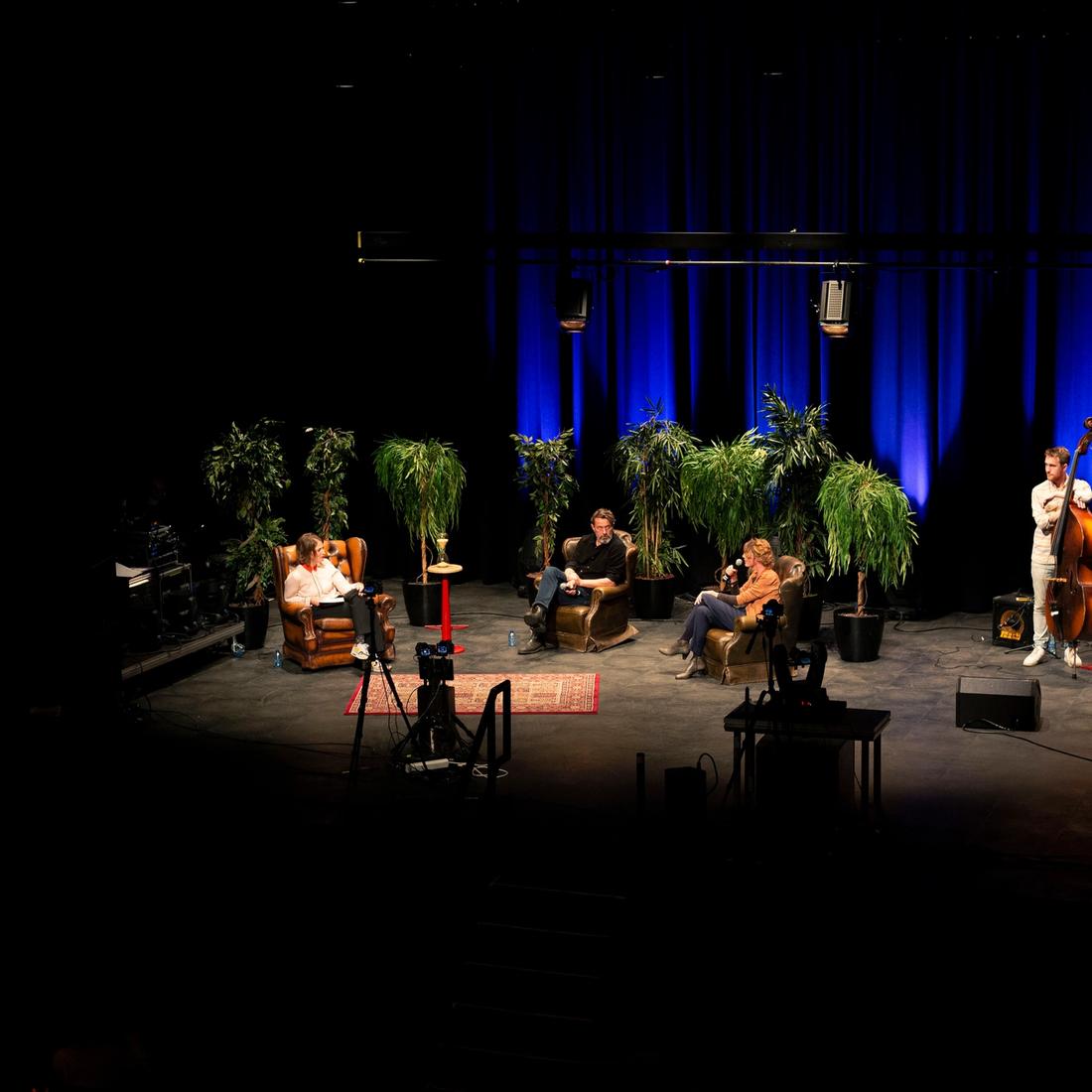 Foto van het podium, met daarop drie mensen en een band
