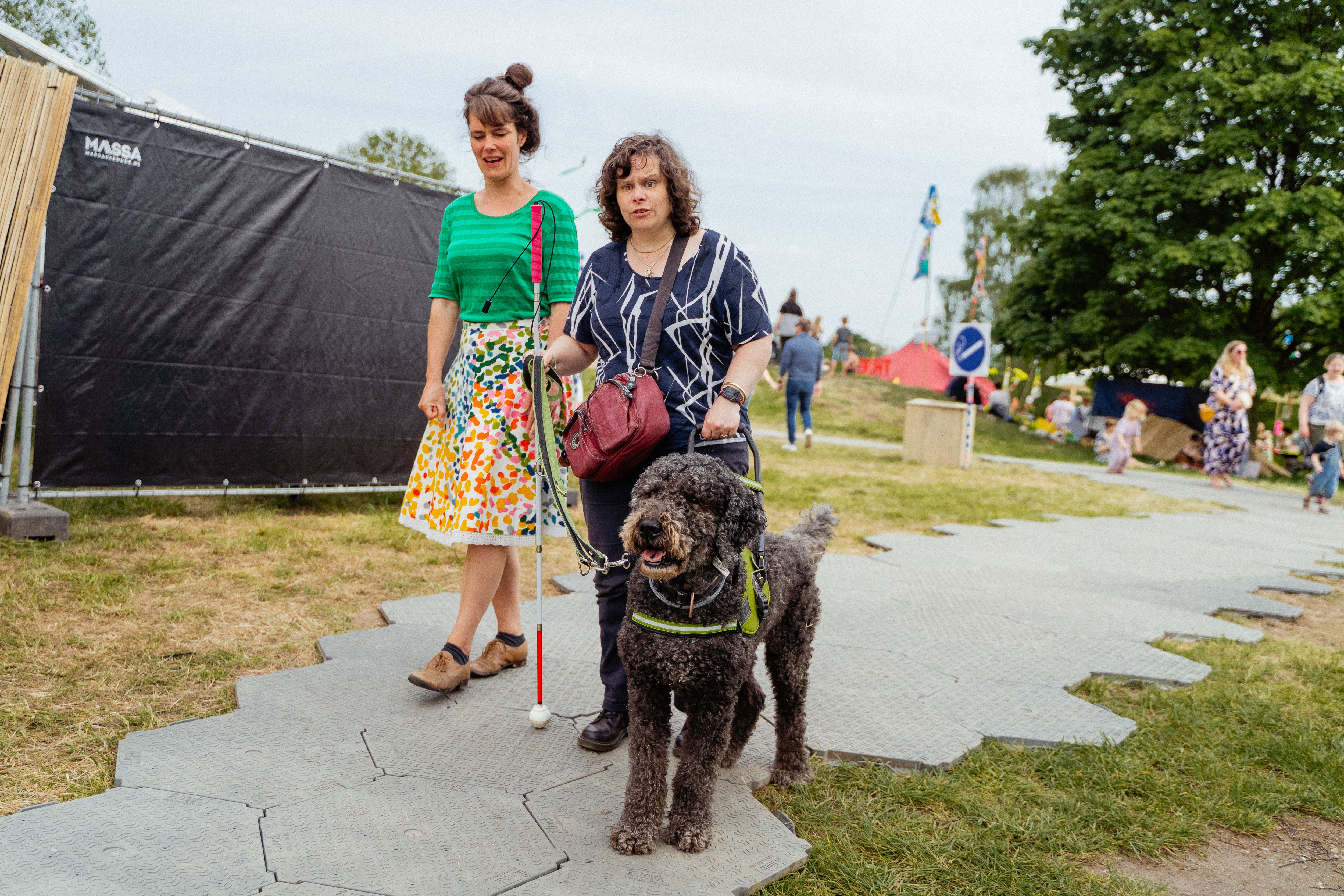 Een vrouw die een festival bezoekt met hulphond en geleidestok