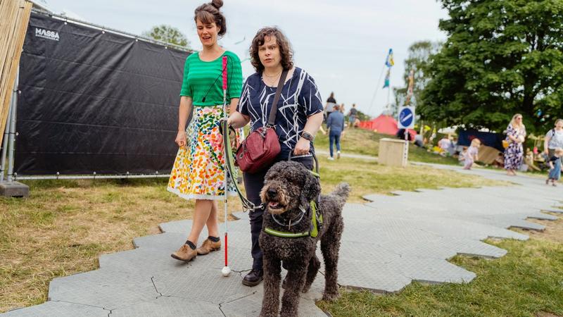 Een vrouw die een festival bezoekt met hulphond en geleidestok