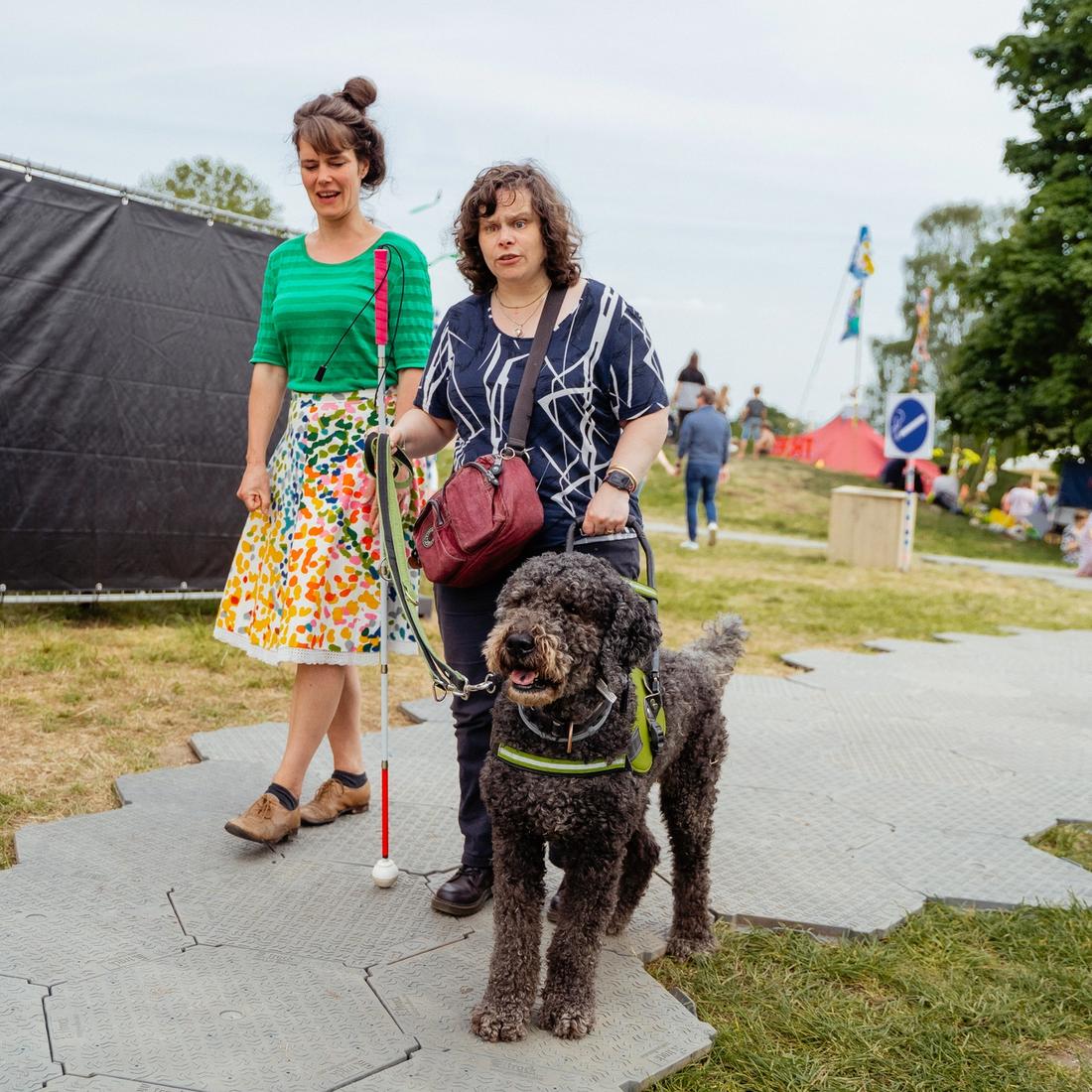 Een vrouw die een festival bezoekt met hulphond en geleidestok