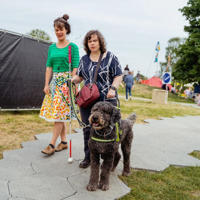 Een vrouw die een festival bezoekt met hulphond en geleidestok