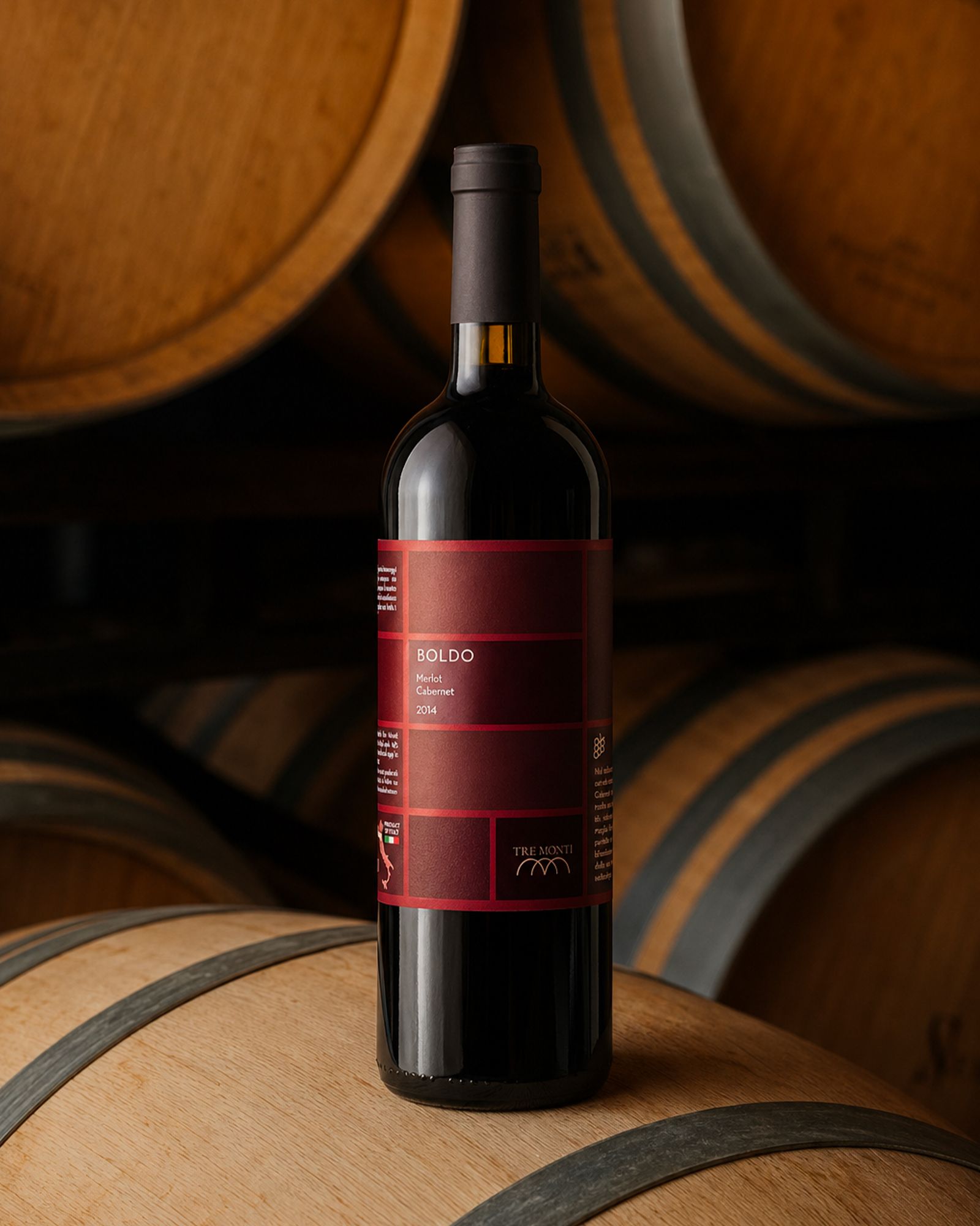 A bottle of Tre Monti Boldo Merlot Cabernet 2014 resting on a wooden barrel in the cellar.