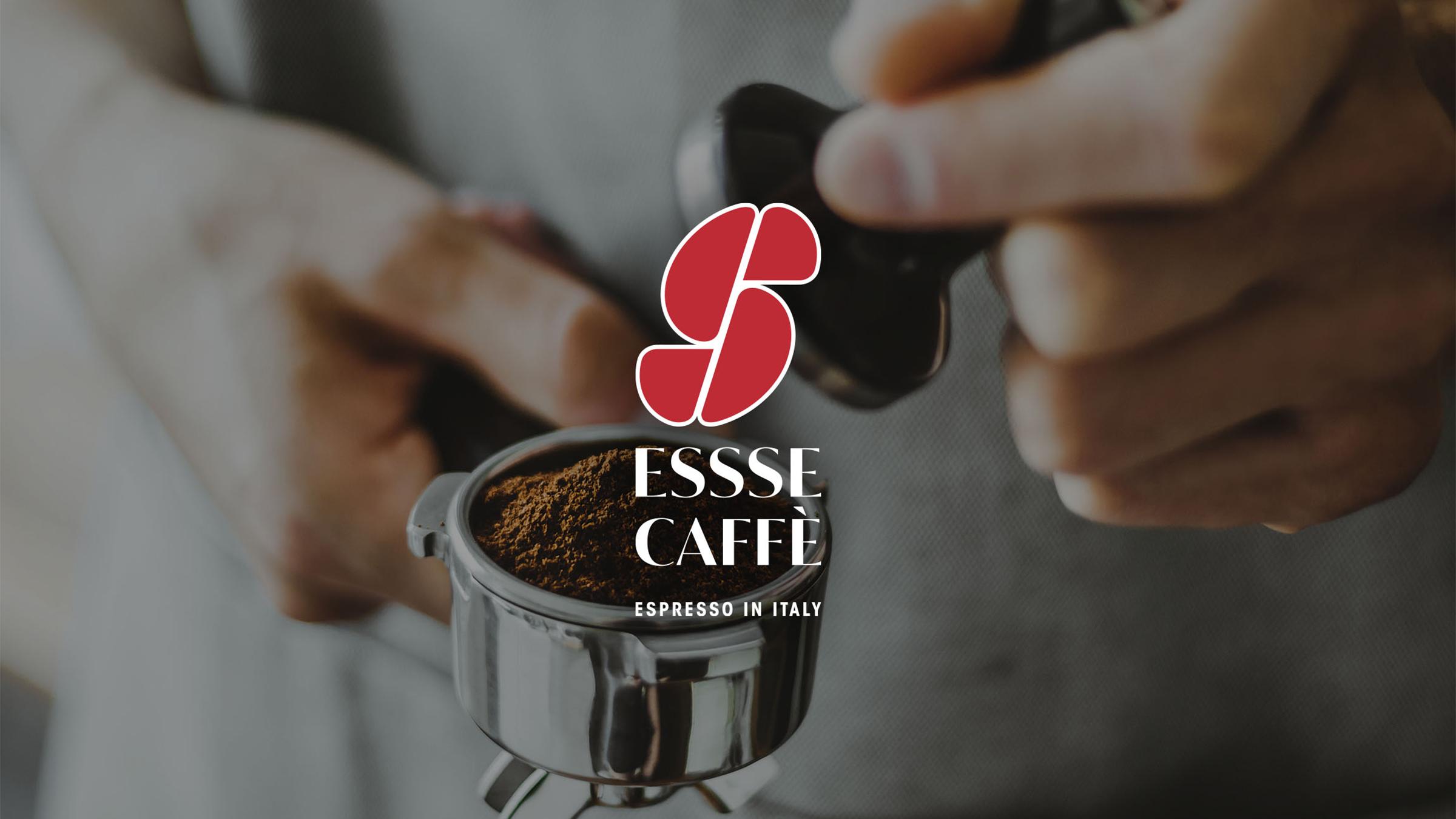 immagine-sfocata-di-un-barista-che-prepara-un-espresso-in-primo-piano-un-portafiltro-pieno-di-caffè-macinato-mentre-una-mano-sta-per-pressarlo-al-centro-il-logo-rosso-e-bianco-di-essse-caffè-con-la-scritta-bianca-espresso-in-italy