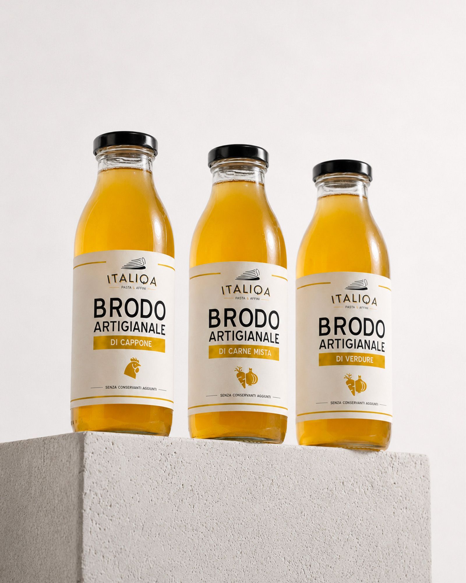 Three bottles of Italiqa artisan broth — capon, mixed meat and vegetable — on a white pedestal.