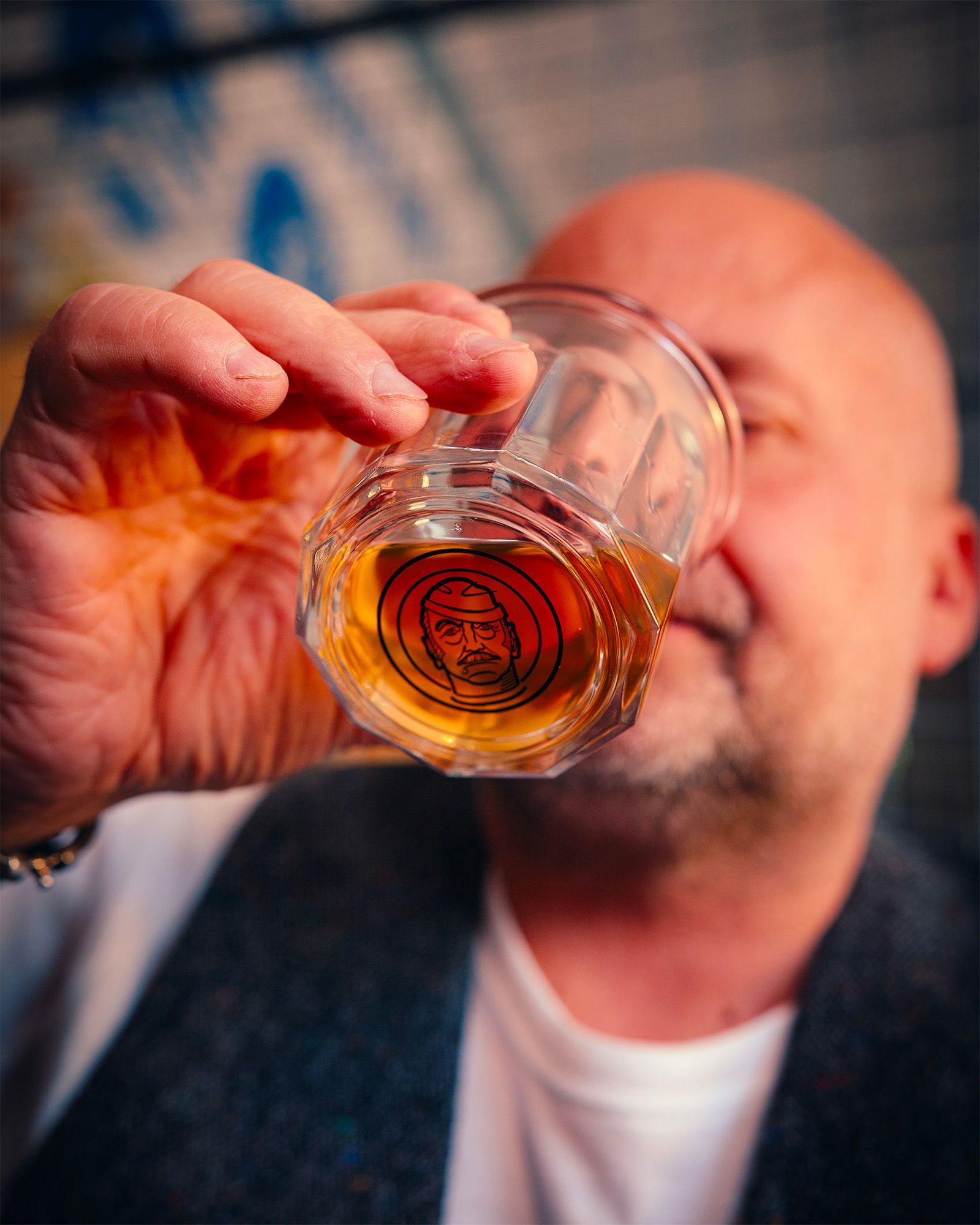 Man drinking an amber spirit from a glass with the Il Signor Camillo logo in close-up