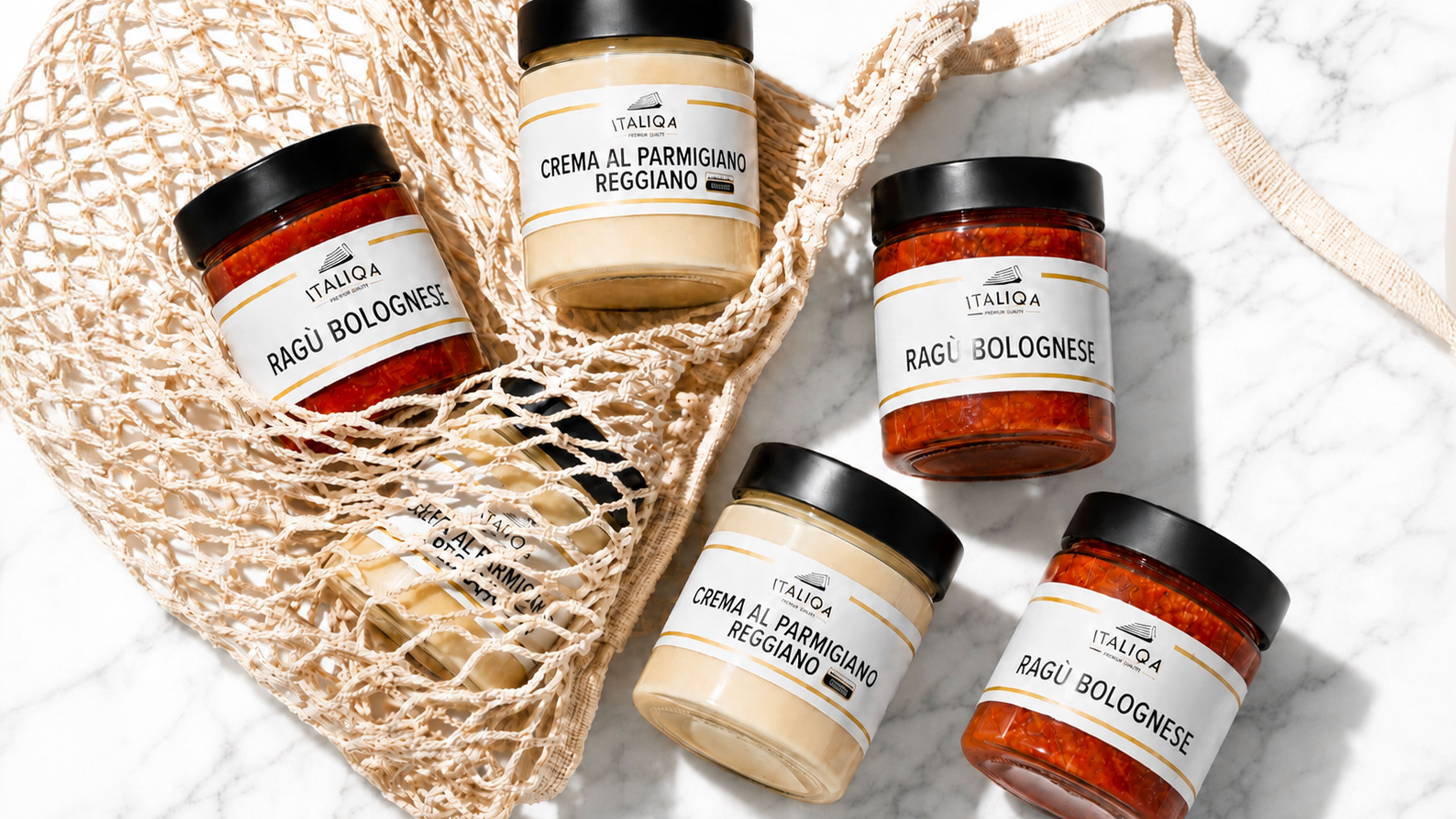 Jars of Italiqa Bolognese ragù and Parmigiano Reggiano cream arranged with a shopping net on a white marble surface.
