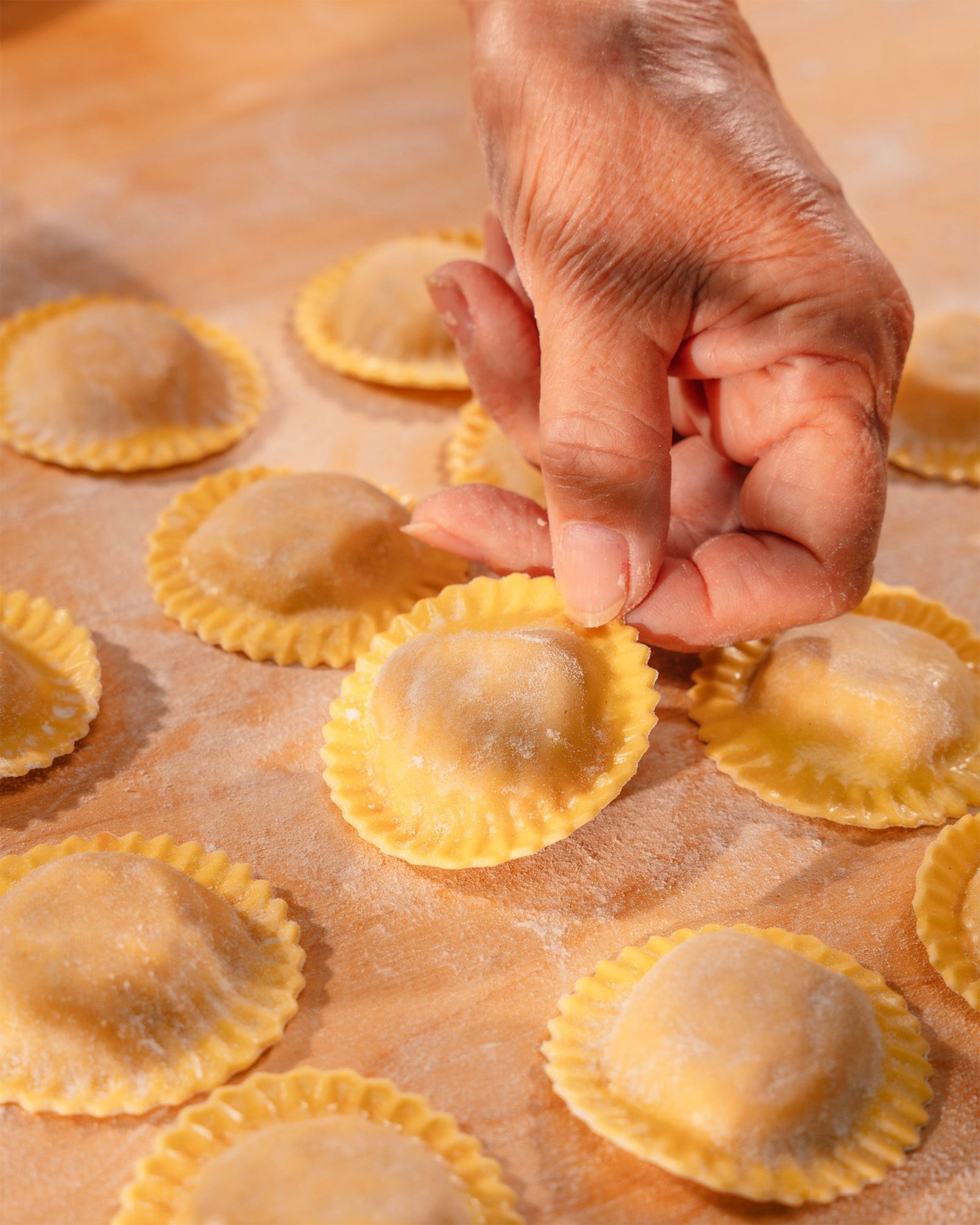 Elderly hand picking up a fresh egg pasta ravioli laid out on a floured wooden pastry board