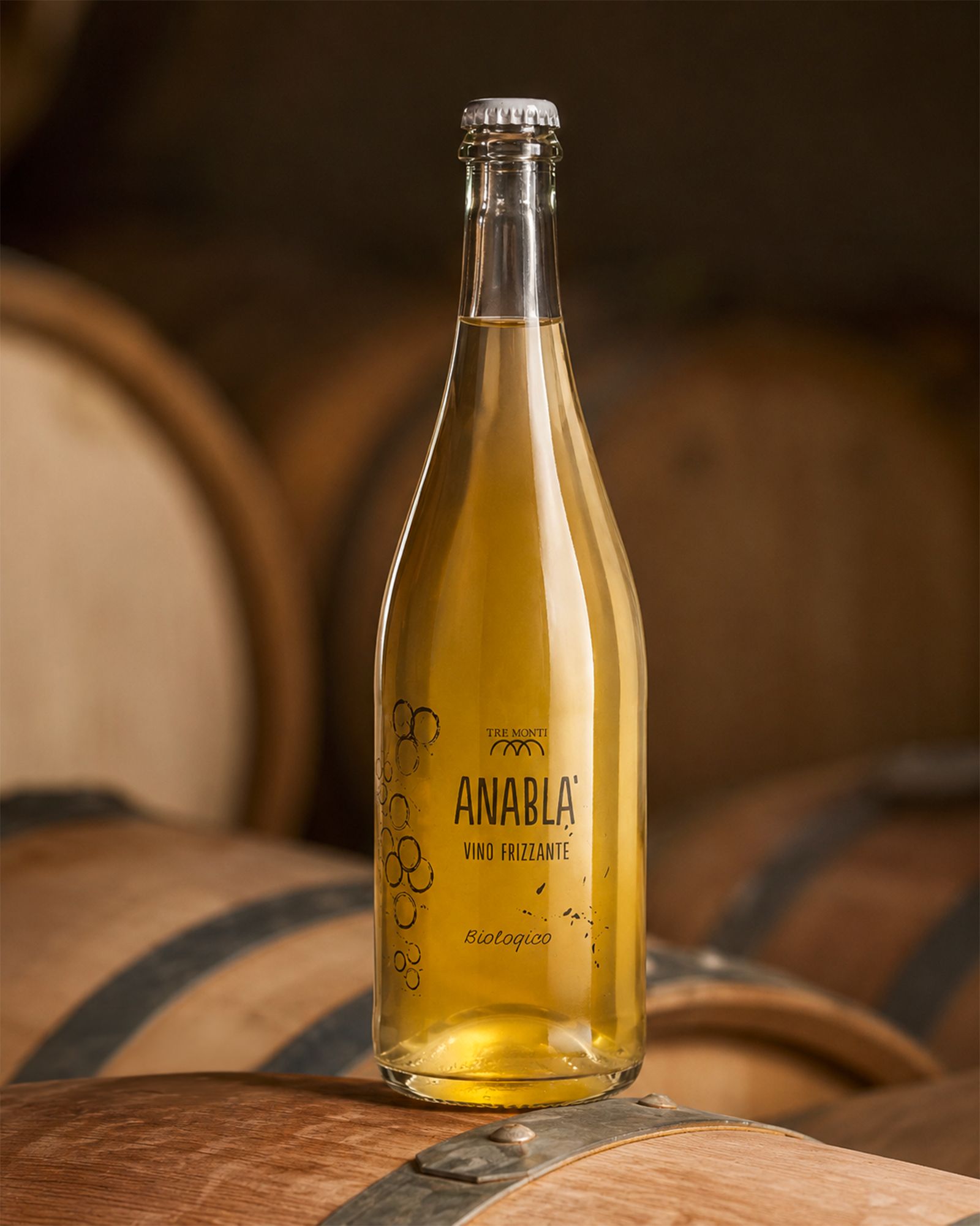 A bottle of Tre Monti Anabla organic sparkling wine resting on a wooden barrel in the cellar.