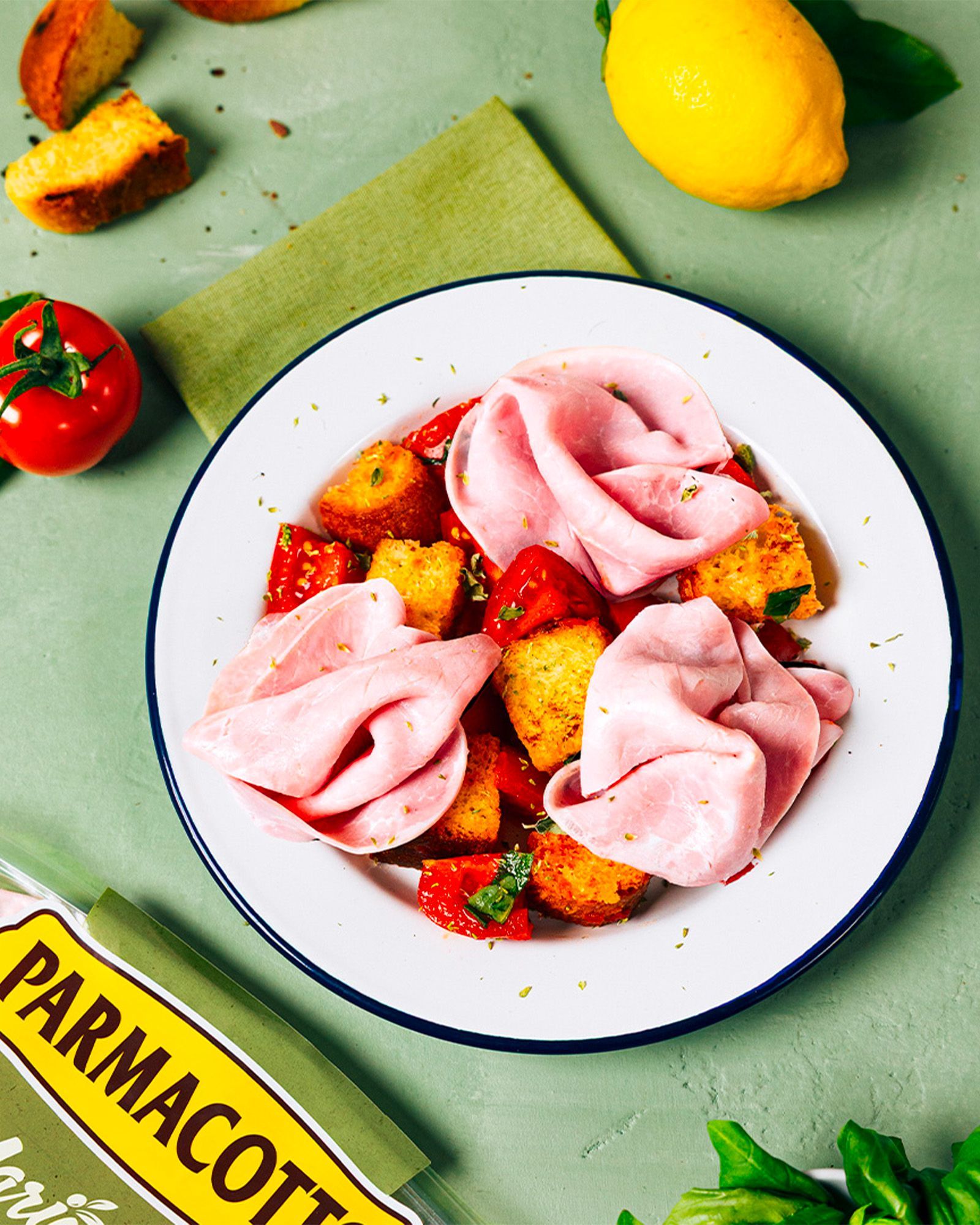 Panzanella salad with Parmacotto cooked ham, cherry tomatoes, croutons, lemon, and basil on a white plate