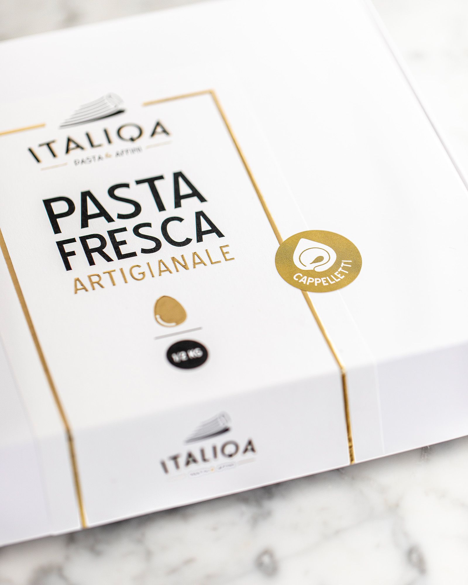 Detail of the white and gold pack of Italiqa artisan fresh pasta, cappelletti, on a marble surface.