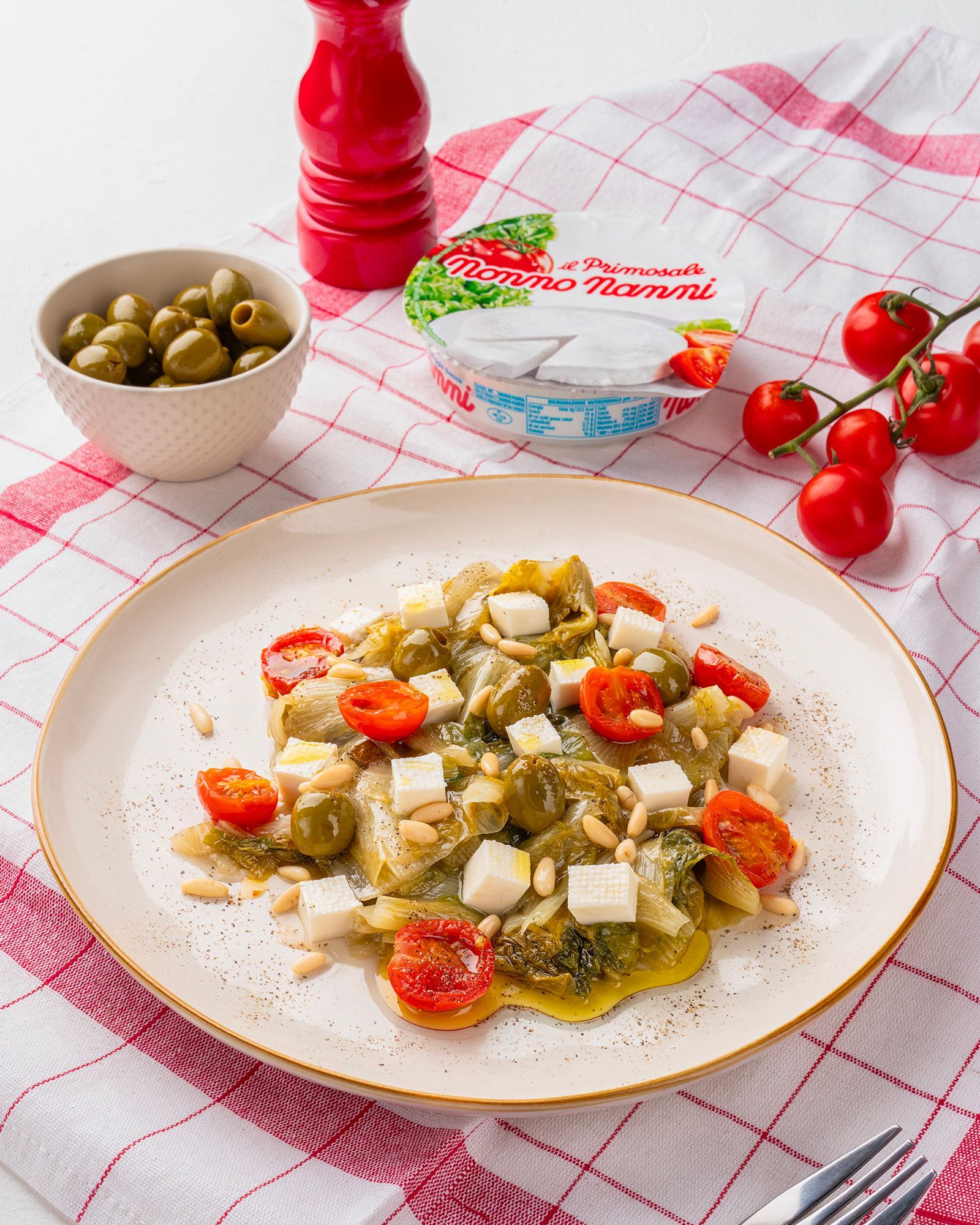 Escarole salad with Nonno Nanni Primosale cheese, cherry tomatoes, olives and pine nuts, on a red checkered tablecloth.