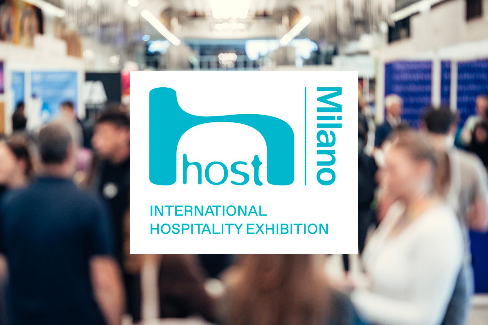 logo-host-milano-international-hospitality-exhibition-su-sfondo-sfocato-di-una-fiera-piena-di-persone