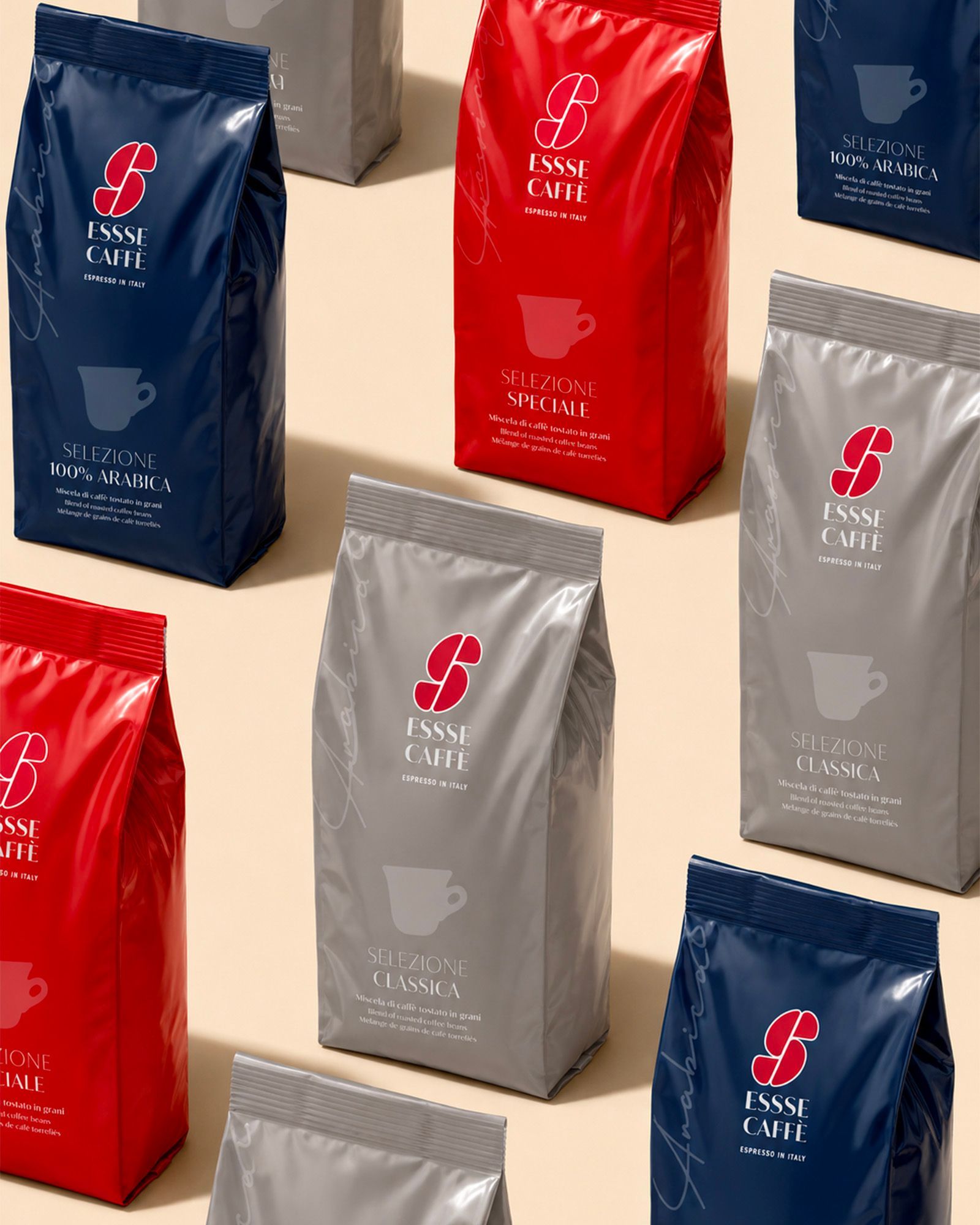 An overhead view of several bags of Essse Caffè whole bean coffee neatly arranged on a light surface. The packs show the brand logo and the different blends color-coded: dark blue for 100% Arabica, red for Selezione Speciale and grey for Selezione Classica.