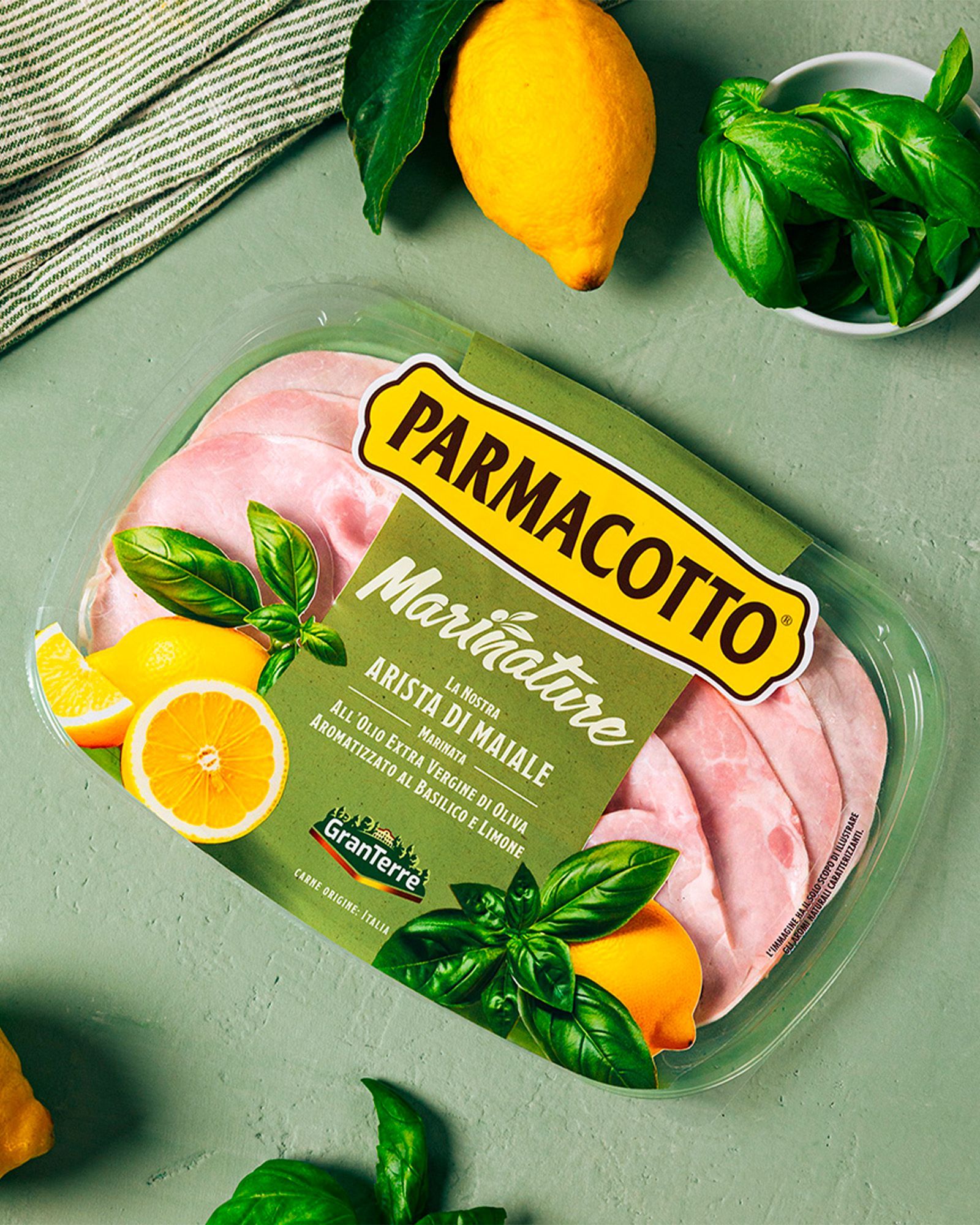 Parmacotto Marinature pack of basil-and-lemon flavored pork loin, with citrus fruit and basil leaves on a green background