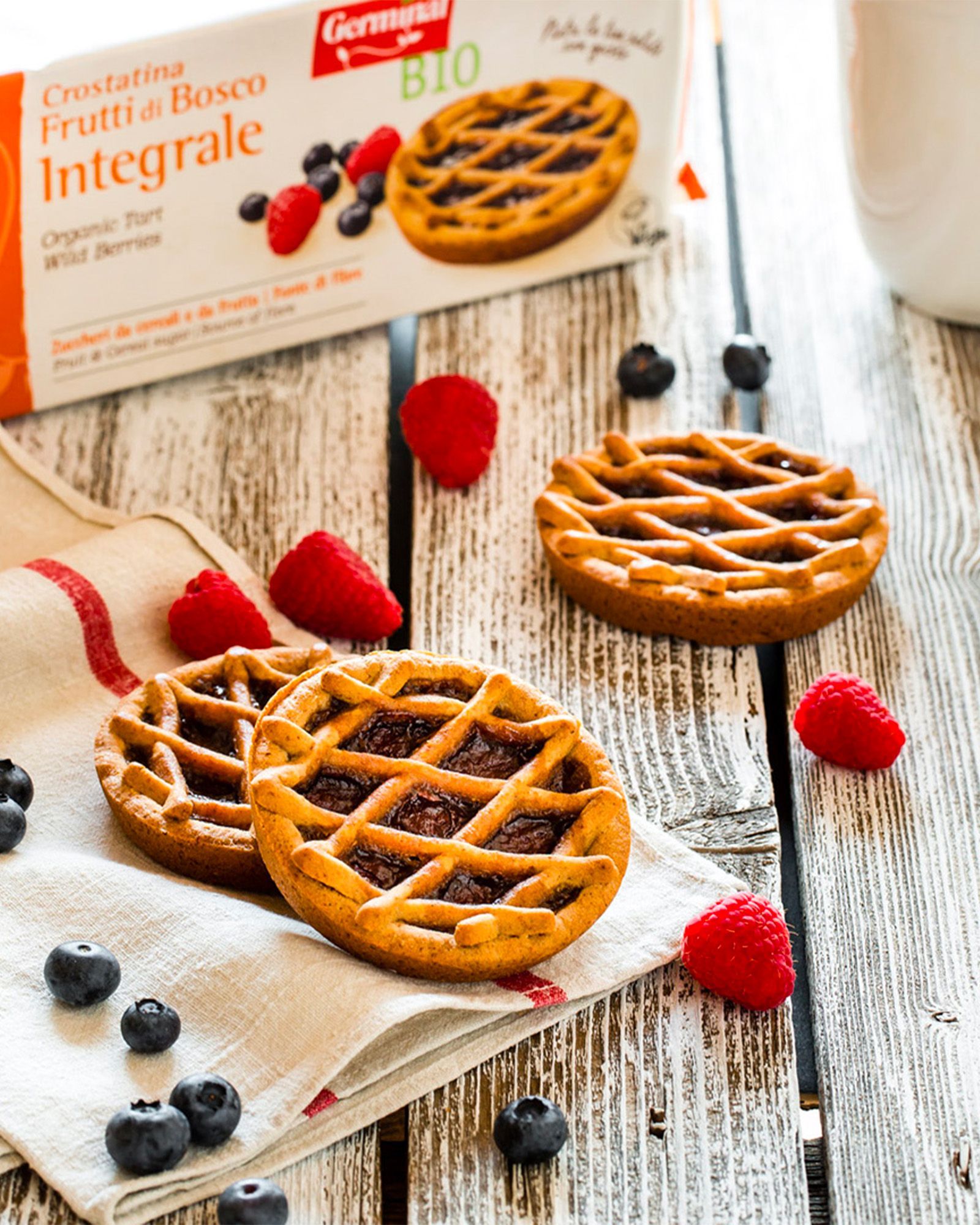 Wholegrain mixed berry tarts with raspberries and blueberries next to a Germinal Bio pack on a wooden table