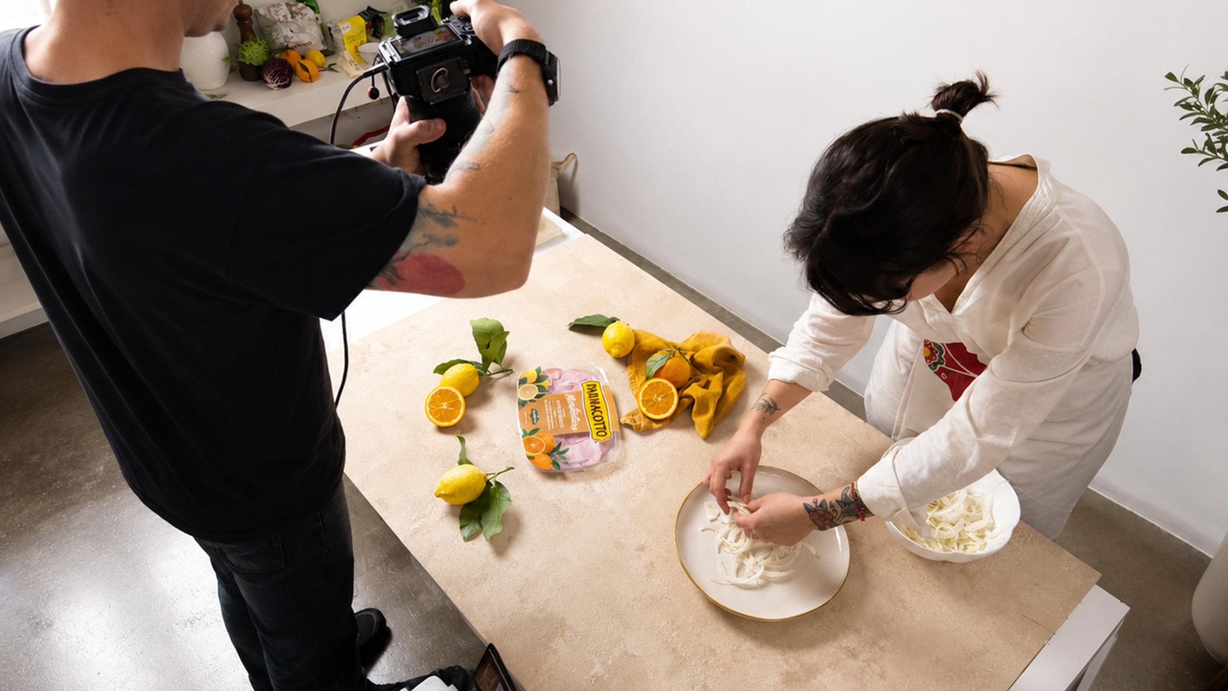 immagine-di-un-fotografo-che-fa-una-foto-ad-una-ragazza-che-impasta-su-un-tavolo-di-legno-con-limoni-e-un-prodotto-sul-tavolo-in-uno-studio