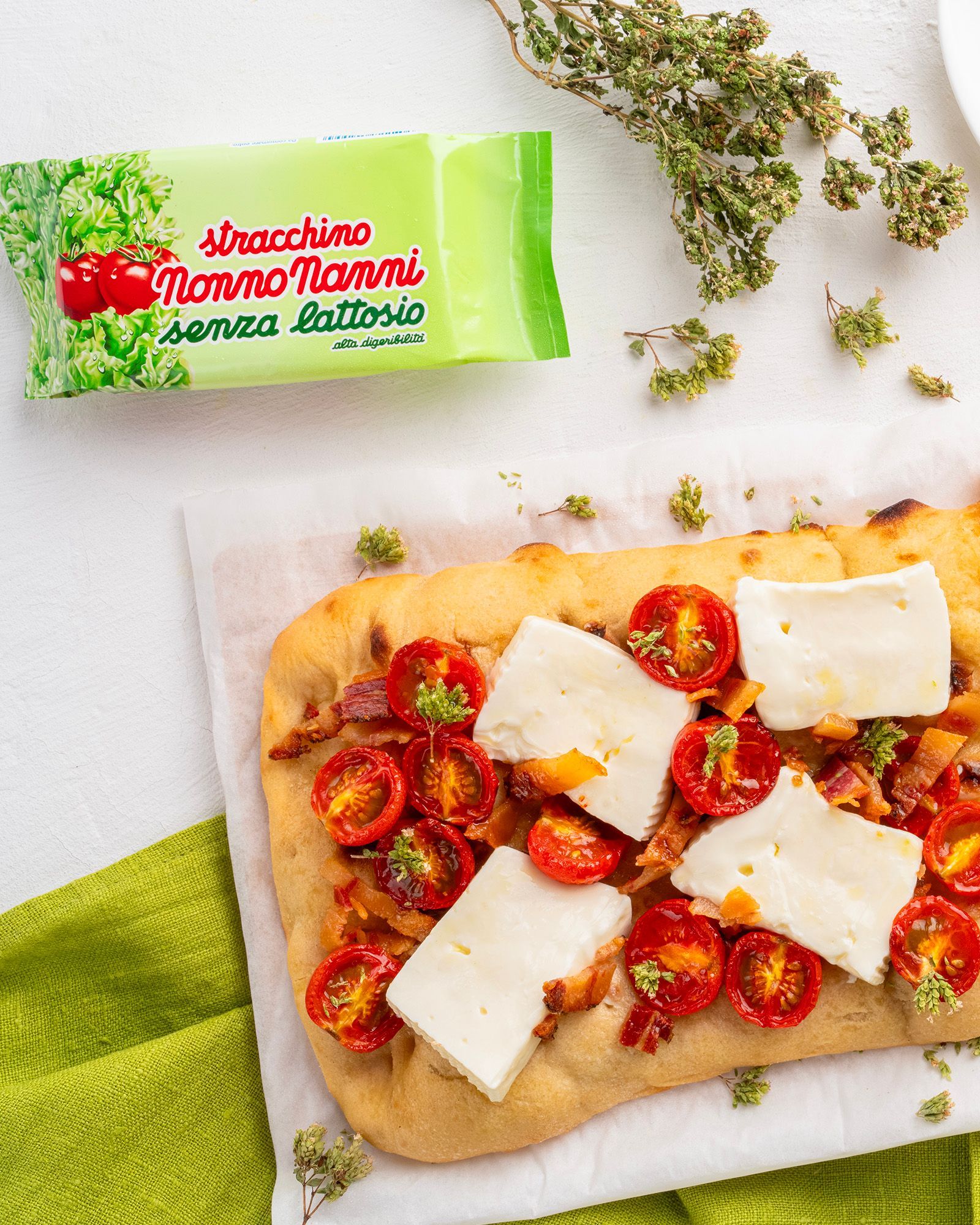 Focaccia with Nonno Nanni lactose-free stracchino, cherry tomatoes and pancetta, on a green napkin.