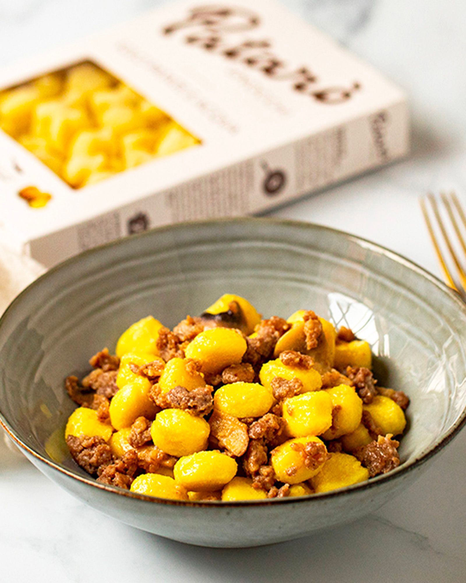 Gnocchi with meat ragù in a grey bowl, with the product pack blurred in the background.
