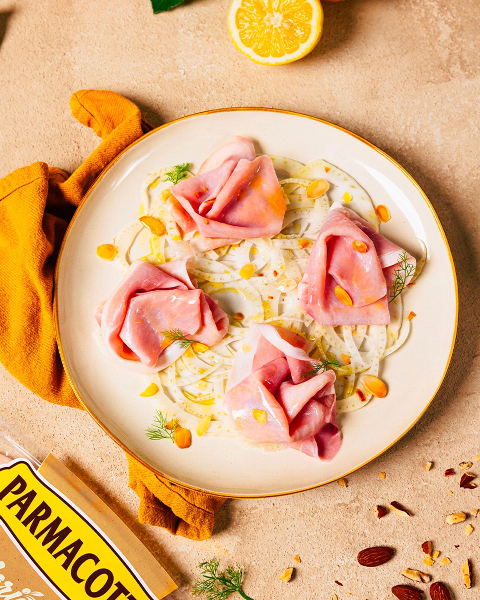 Fennel salad with mortadella, almonds, lemon, and dill on a plate, with a Parmacotto pack partially visible