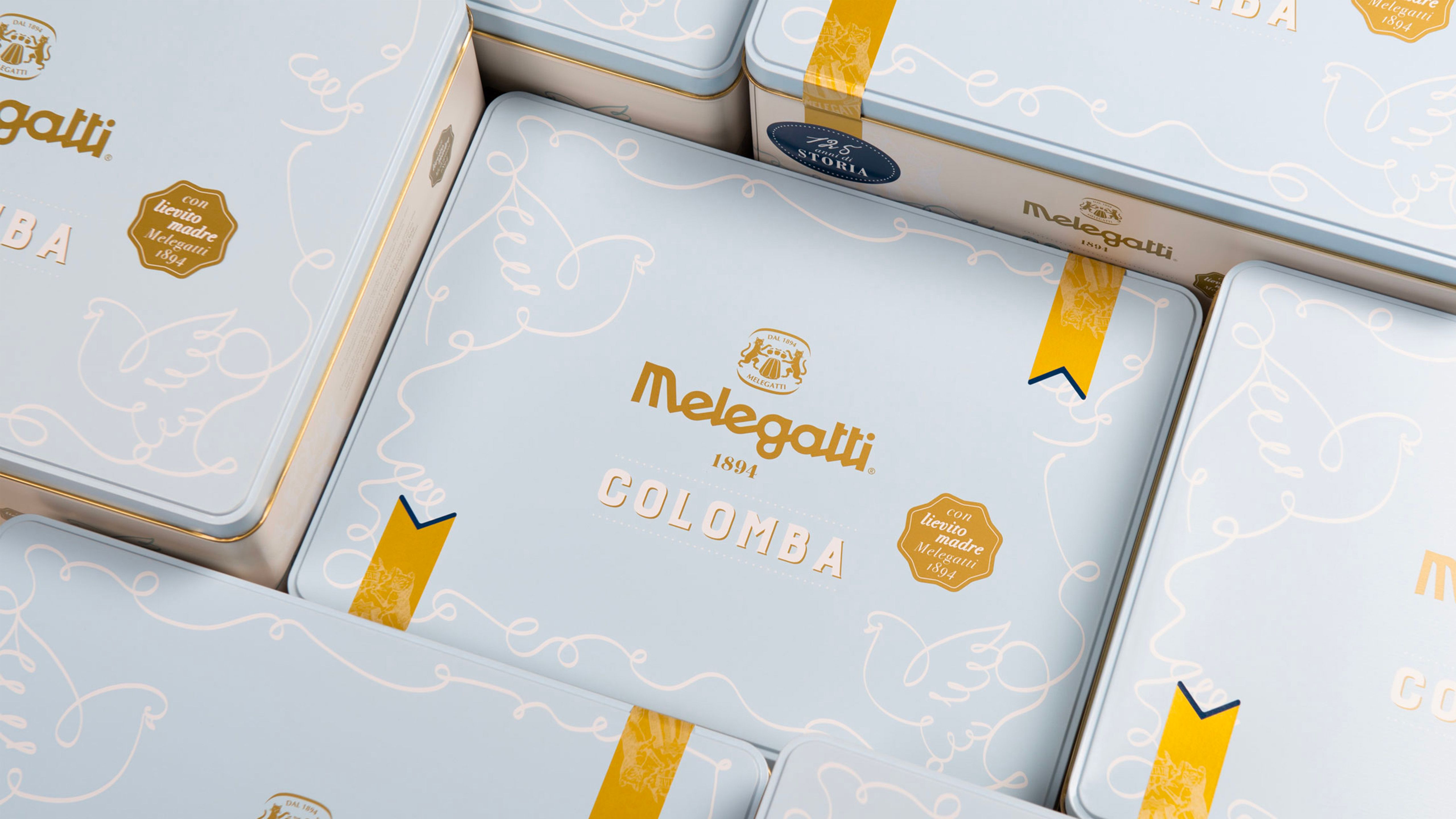 Melegatti Colomba packs in light-blue tins with gold details and linear decorations, arranged in the foreground.