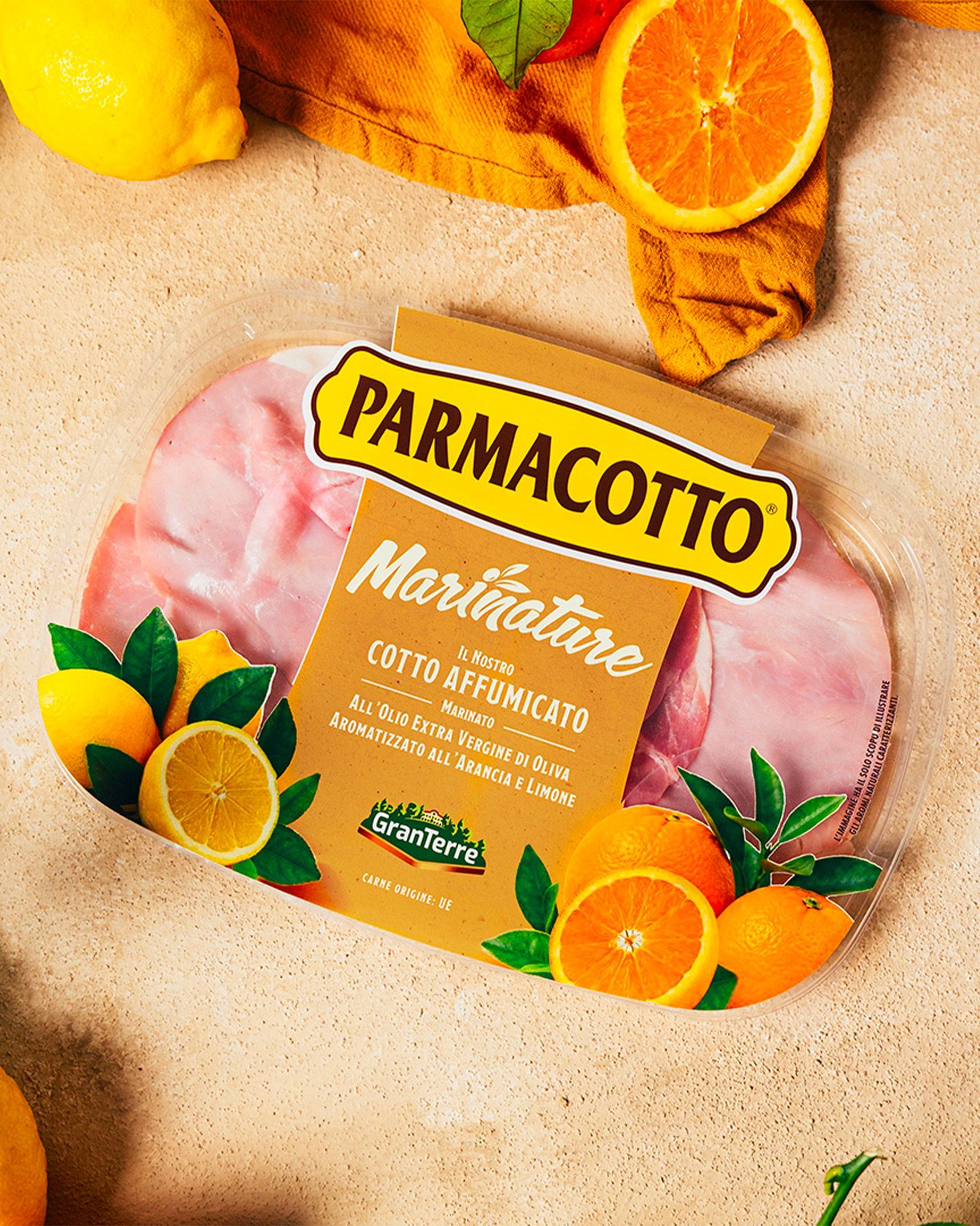 Parmacotto Marinature pack of orange-and-lemon flavored smoked cooked ham, with citrus fruit on a beige background
