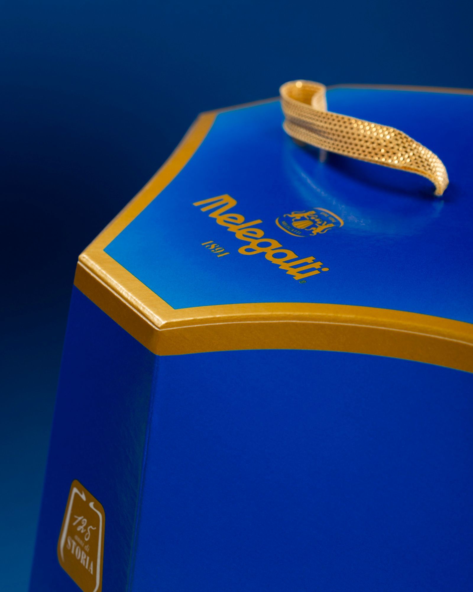 Detail of the blue and gold Melegatti pack with logo and gold handle on a blue background.
