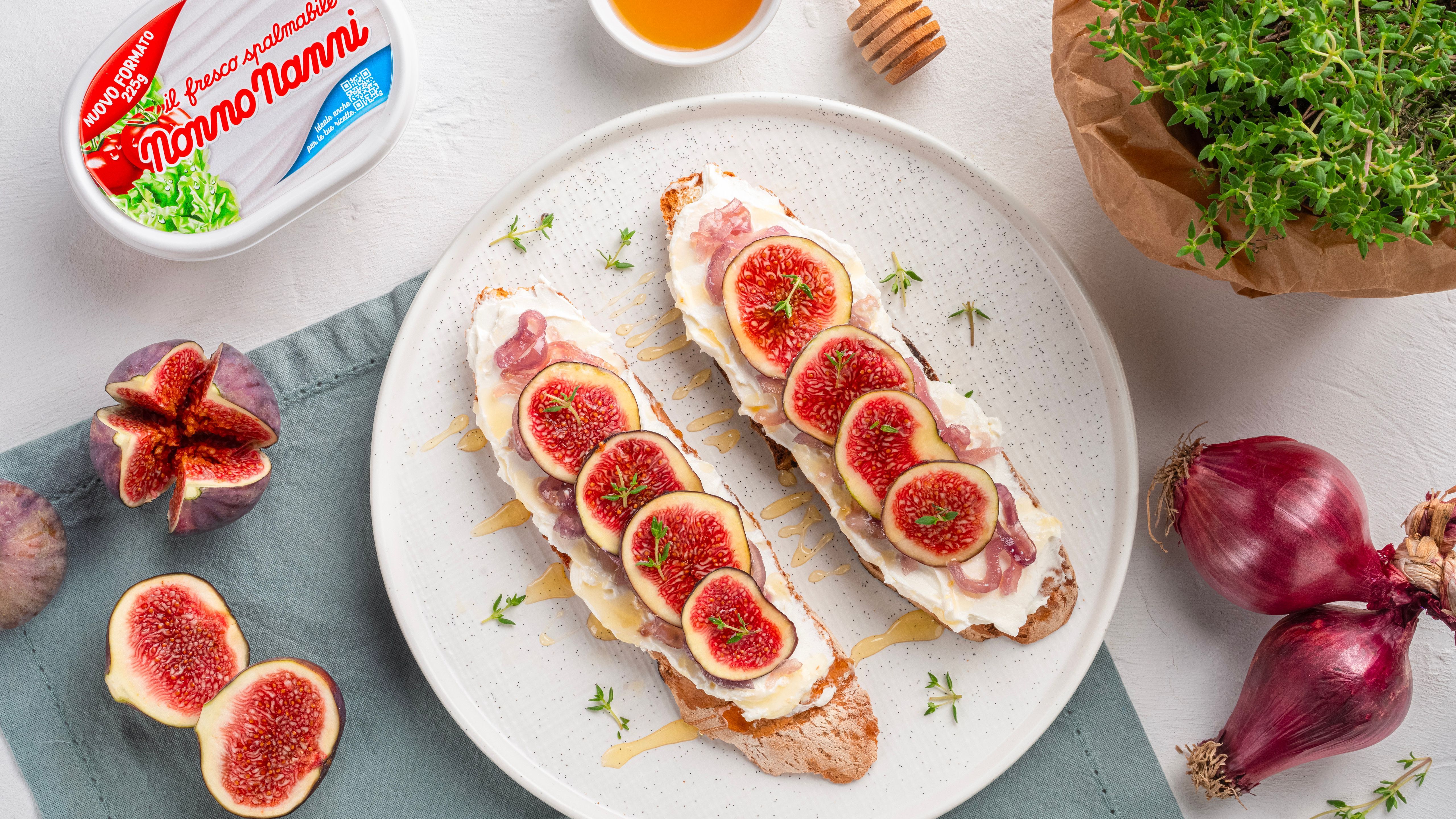 Crostini with fresh cheese, figs, prosciutto and honey on a plate, with a Nonno Nanni pack, red onions and thyme.
