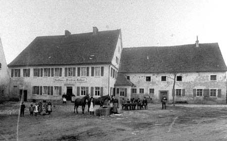 Historische Aufnahme des Gasthauses Kollmar um 1900: vor dem zweigeschossigen Gebäude stehen Dorfbewohner und Pferde auf dem unbefestigten Platz, rechts schließt das Brau- und Wirtschaftsgebäude an.