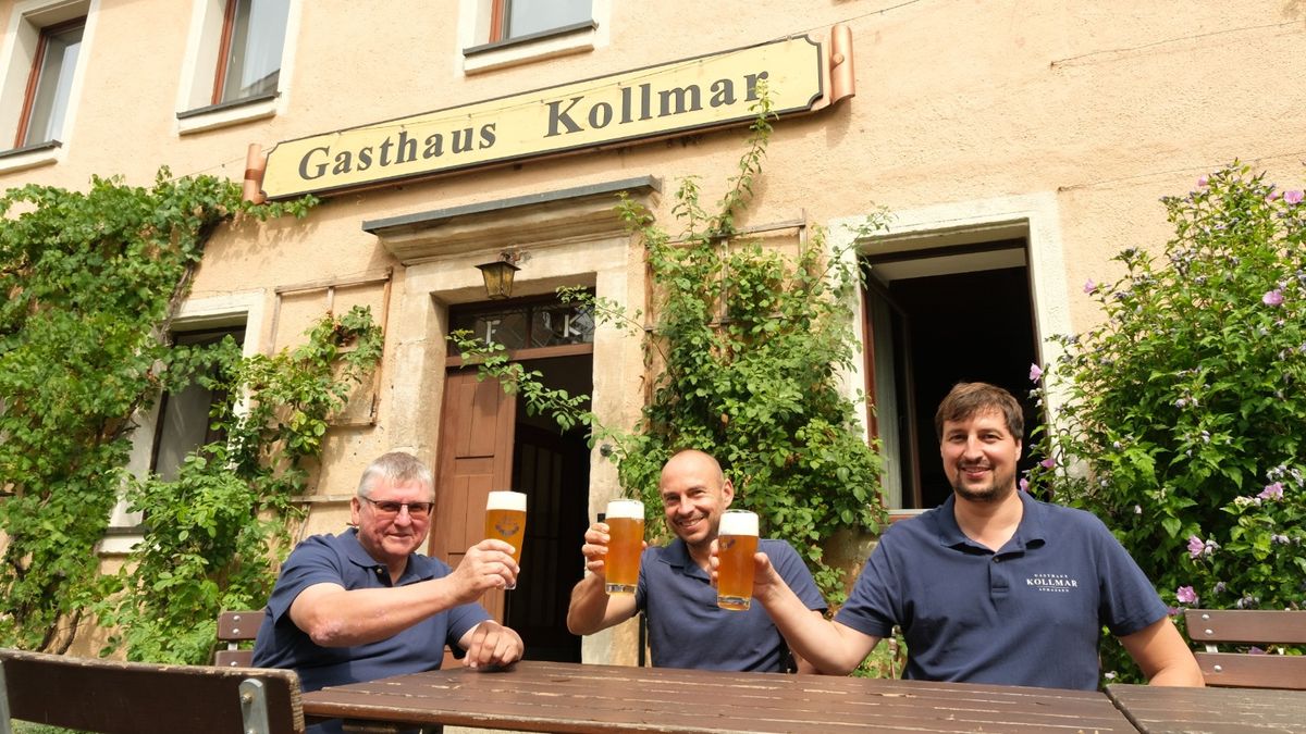 Die drei Wirte stoßen mit Bier vor dem Eingang des Gasthauses Kollmar an, über ihnen das Wirtshausschild.