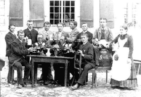 Historische Aufnahme um 1900: eine Runde von Männern mit Bierkrügen an einem Tisch vor dem Wirtshaus, Rechts die Wirtin Margarethe Betz als Bedienung mit weißem Schürzenkleid.