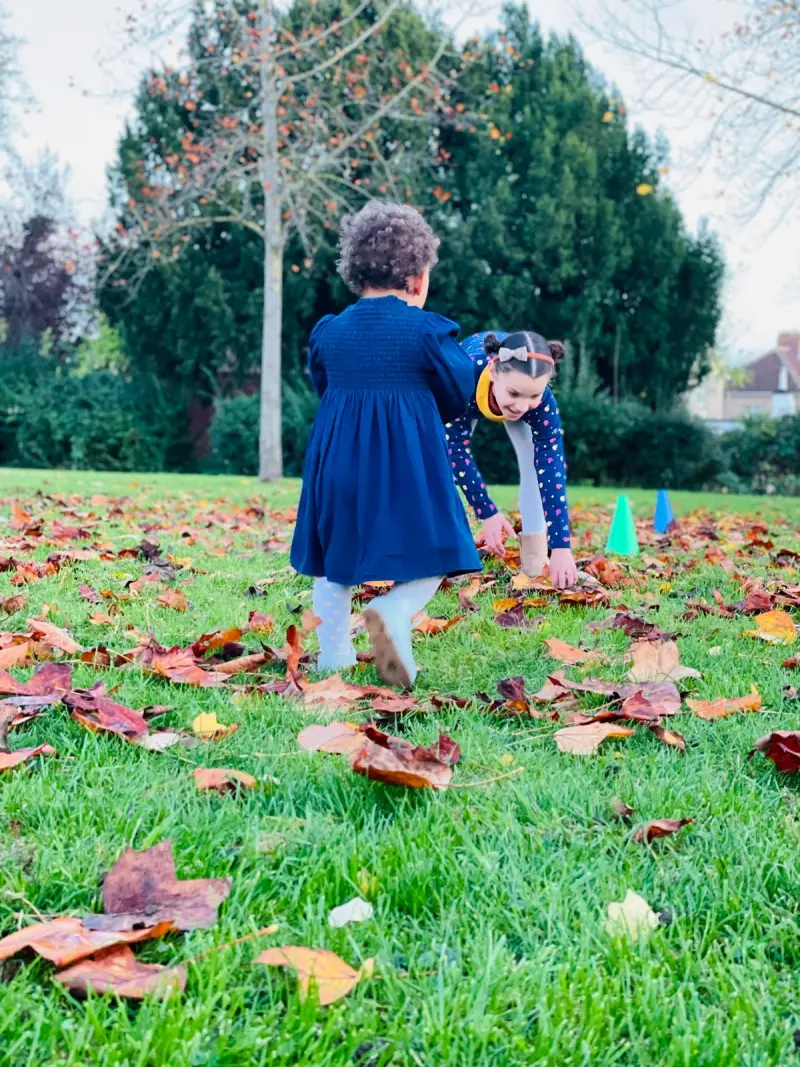 two children playing in autumn leaves on a grassy field