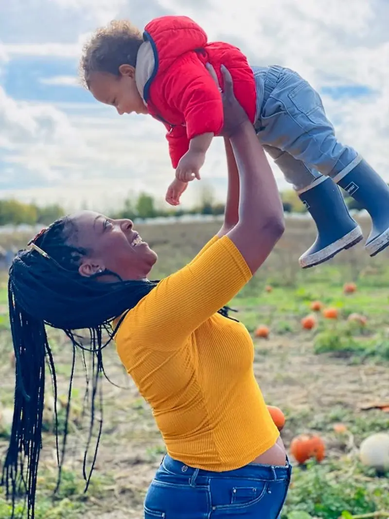 woman joyfully lifts baby in pumpkin patch outdoors