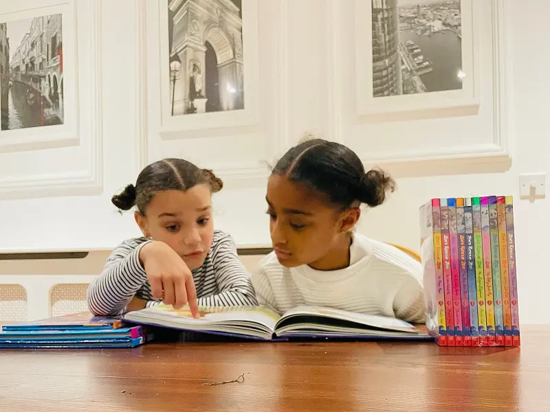 two-girls-reading-a-book-together-at-a-wooden-table