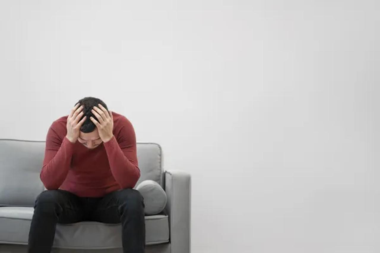a man sitting on a sofa with his head in his hands, appearing stressed or overwhelmed