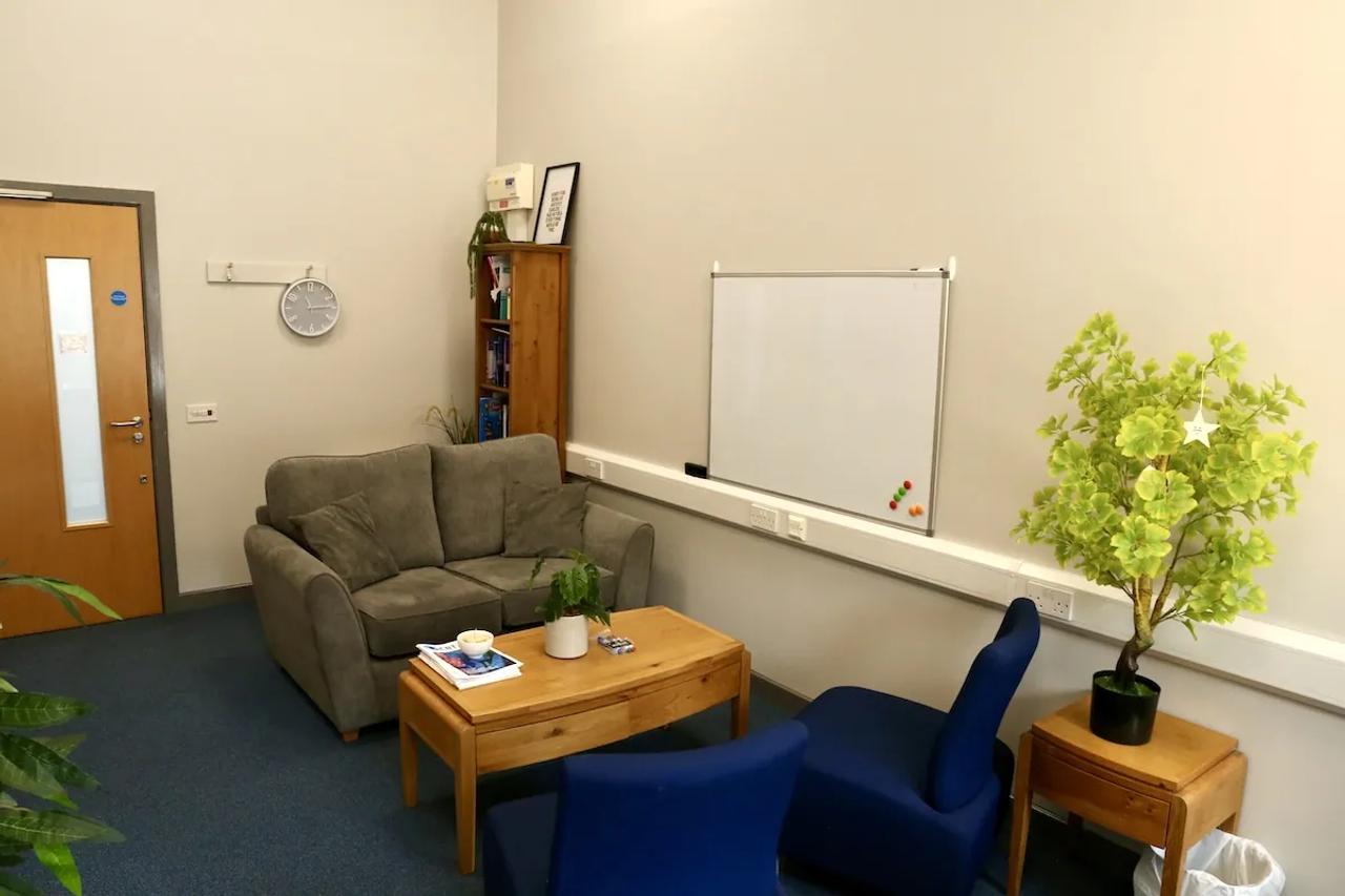 A therapy room with a sofa, two blue armchairs, a bookcase and a whiteboard