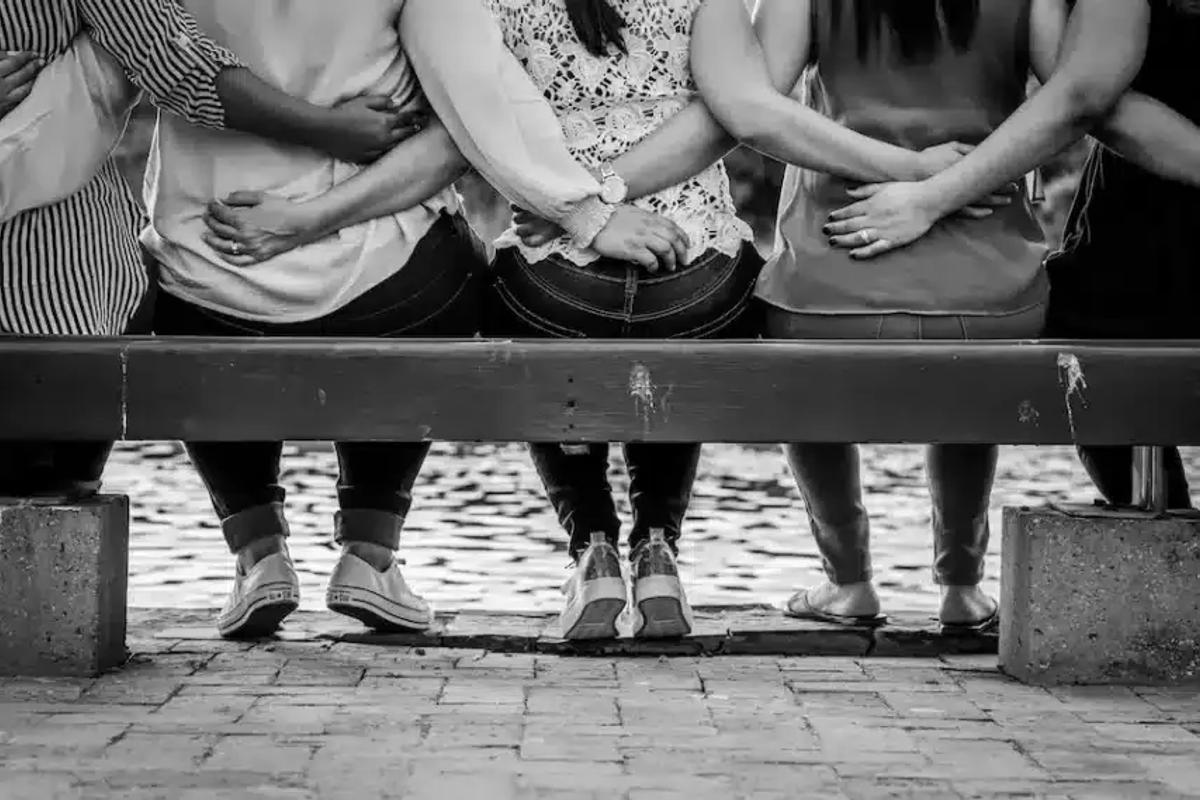 people in enm relationship sat on a bench with arms around each other