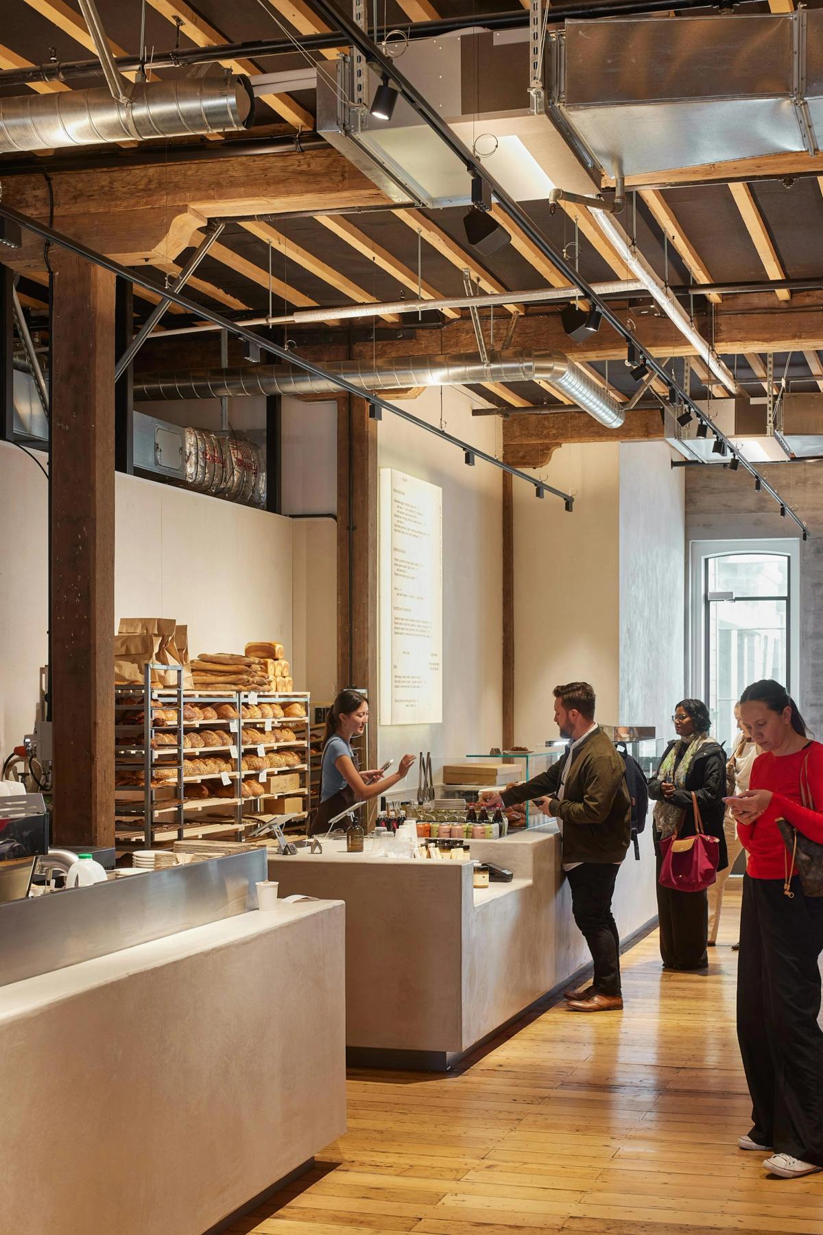 Tadelakt-finished retail counter at Daily Bread Britomart with bread display, menu board, and customers queueing beneath the exposed timber ceiling structure