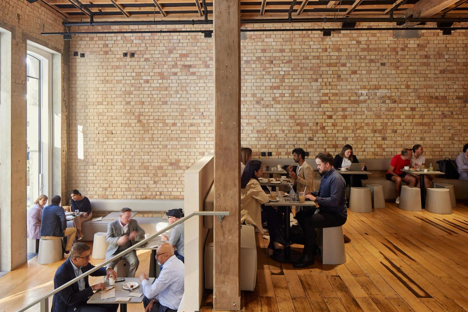 Banquette seating along exposed heritage brick walls at Daily Bread Britomart bakery in Auckland, with kauri timber flooring, jarrah columns, and Daily Plastic Stools by Alasdair Tarry