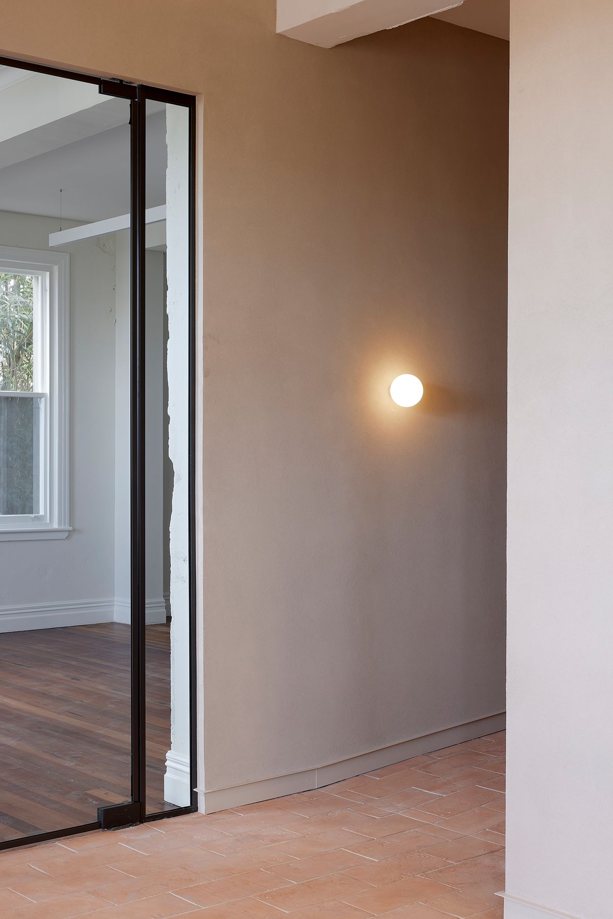 Material detail at The Chambers showing Sto-lit plaster walls in a warm earth tone, handmade terracotta floor tiles in the entrance hallway, and a steel-framed glazed partition opening onto a heritage interior — adaptive reuse by Knight Associates