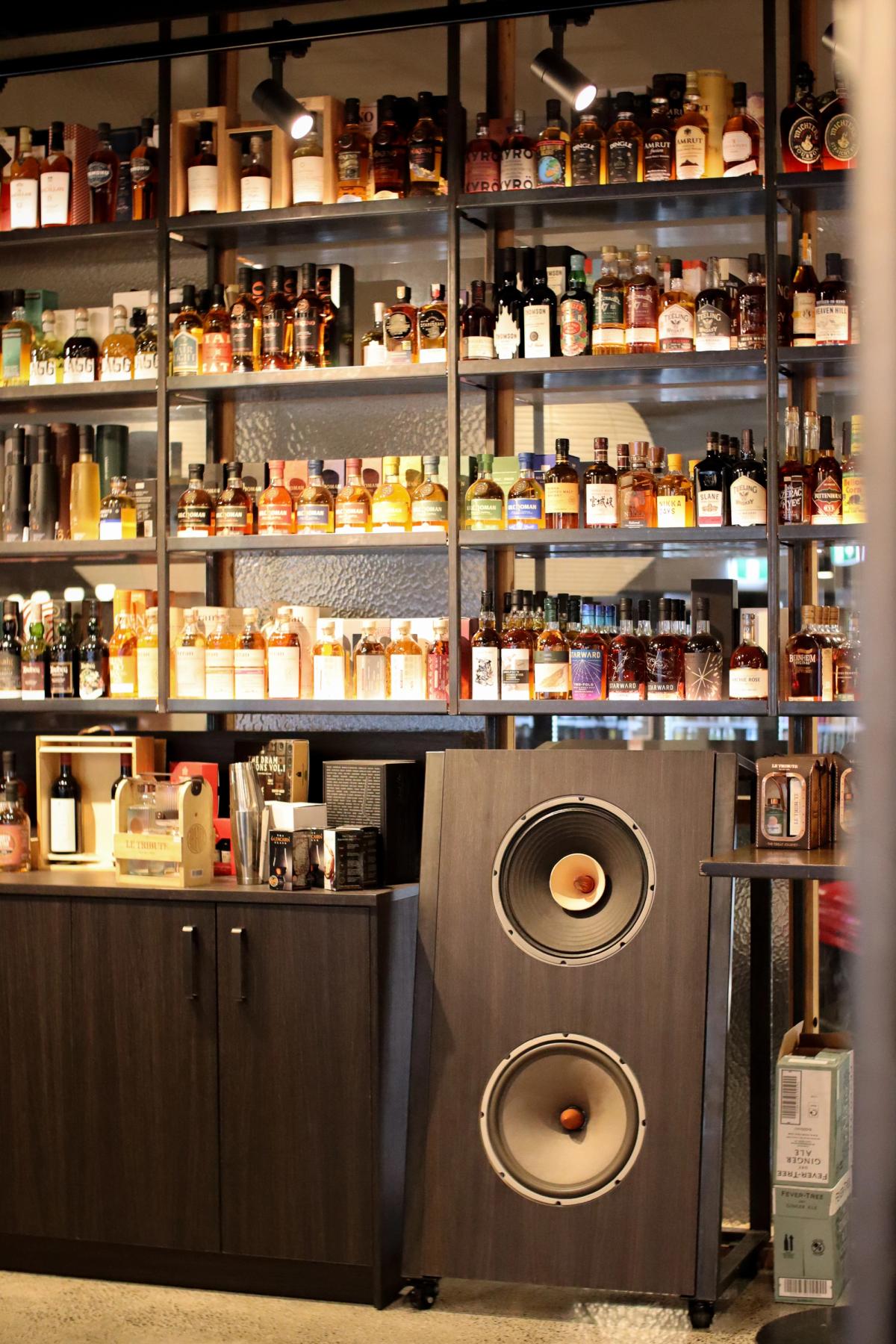 close up photography of display alcohol on steel shelving with custom hi-fi speakers besides display cabinet