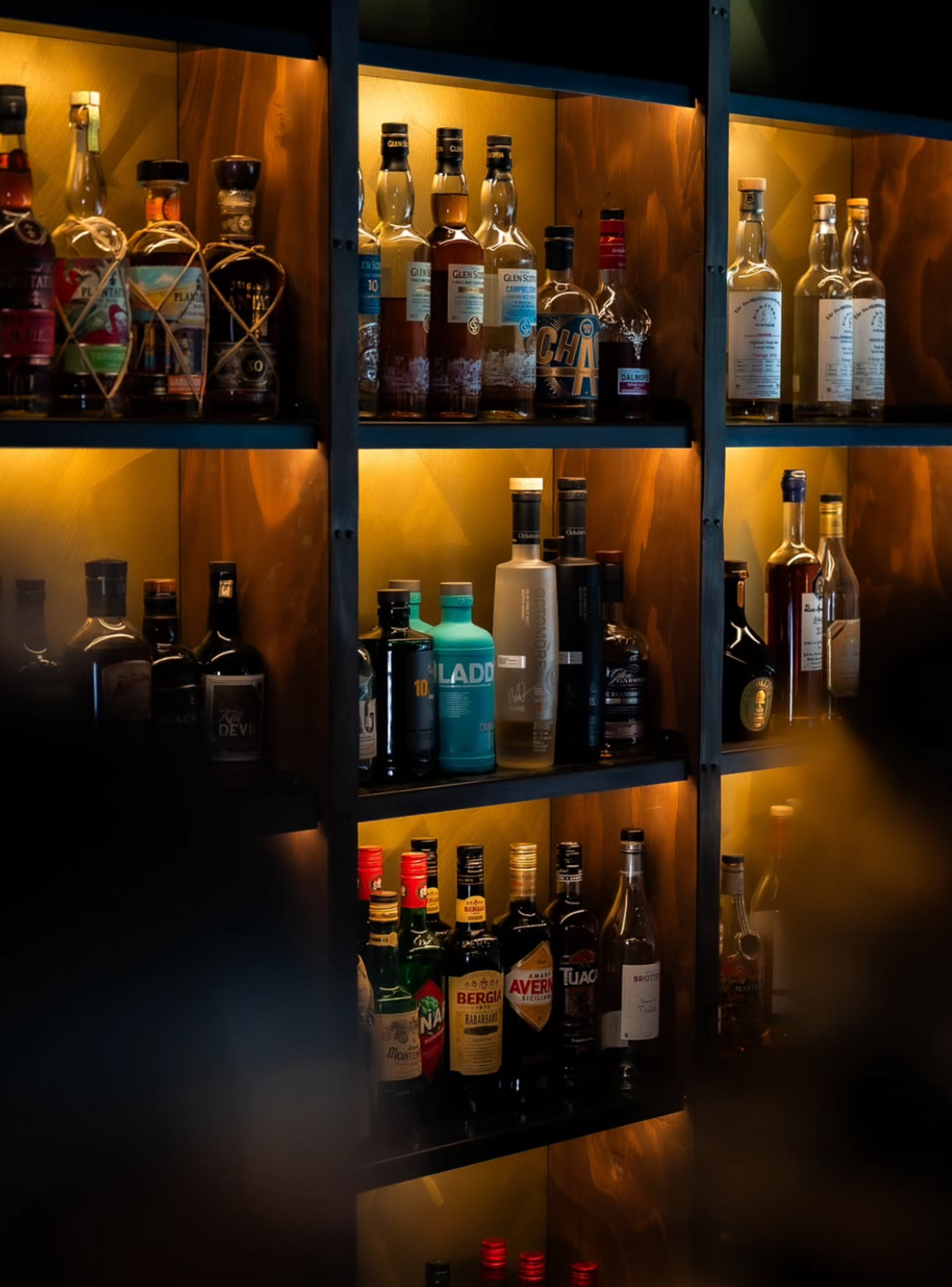 Bottle of alcohol sitting on the custom shelving in a moody speakeasy bar setting with warm lighting