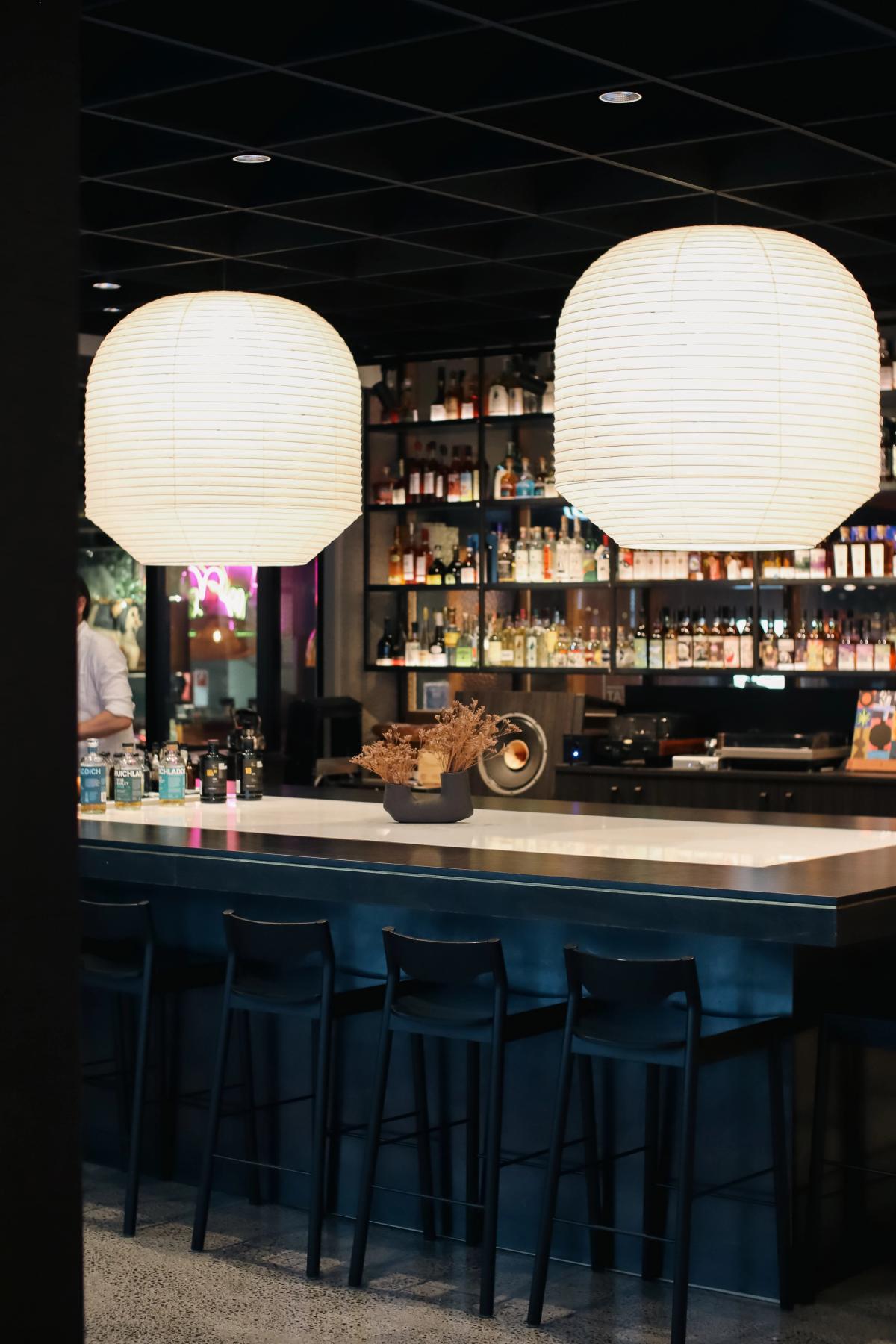 two pendants suspended over an island bar alcohol on steel shelving in the background
