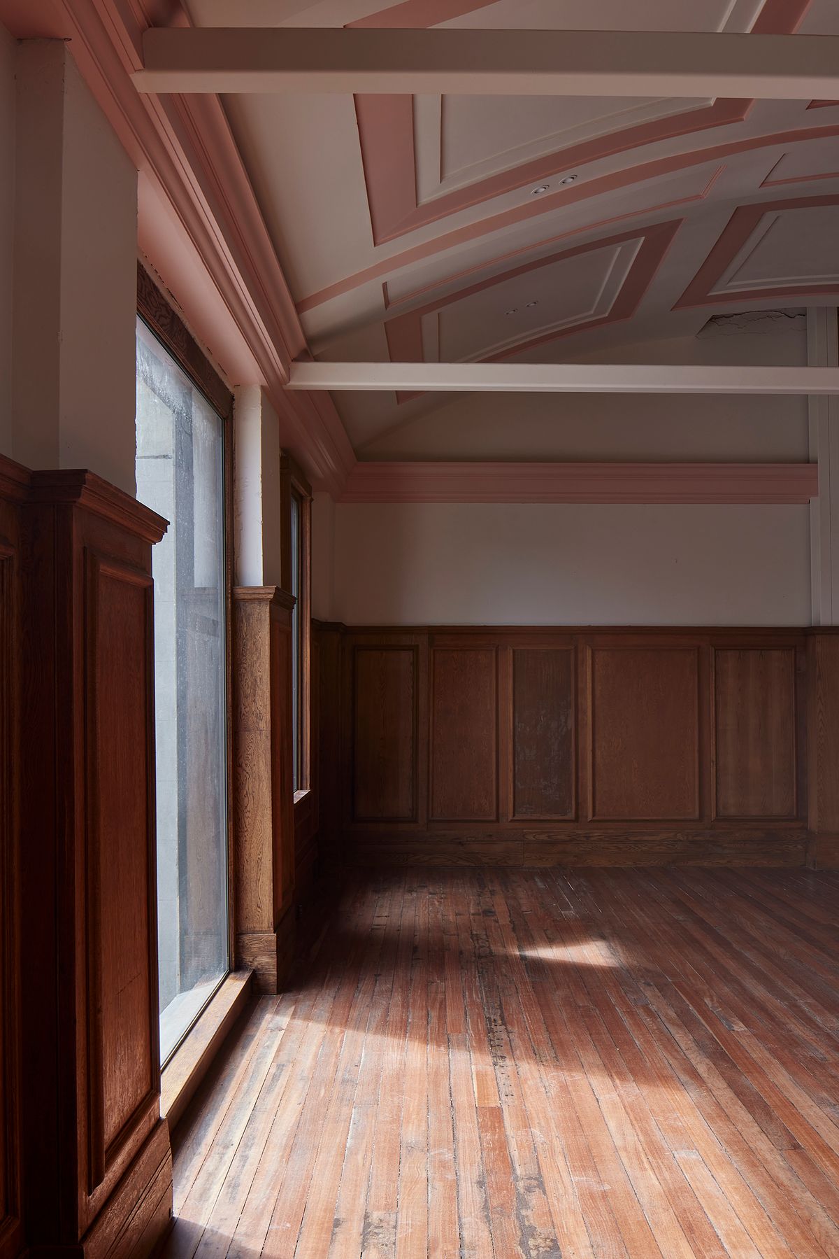 Restored chamber room at The Chambers with intact heritage timber wainscoting, ornate plaster ceiling treated in a pink-and-cream colour palette, and original timber floorboards — adaptive reuse of the 1927 Mount Albert Council building by Knight Associates