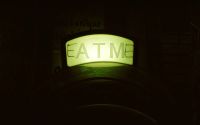 A glowing sign with the words "EAT ME" written on it is illuminated in a dark setting.