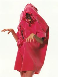 A person is wearing an oversized, bright pink garment with ruffled edges that covers most of their body and head while posing with their hands raised.