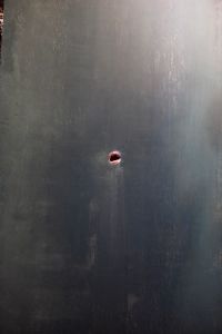 A dark surface with a small hole in the center revealing a glimpse of a reddish interior.