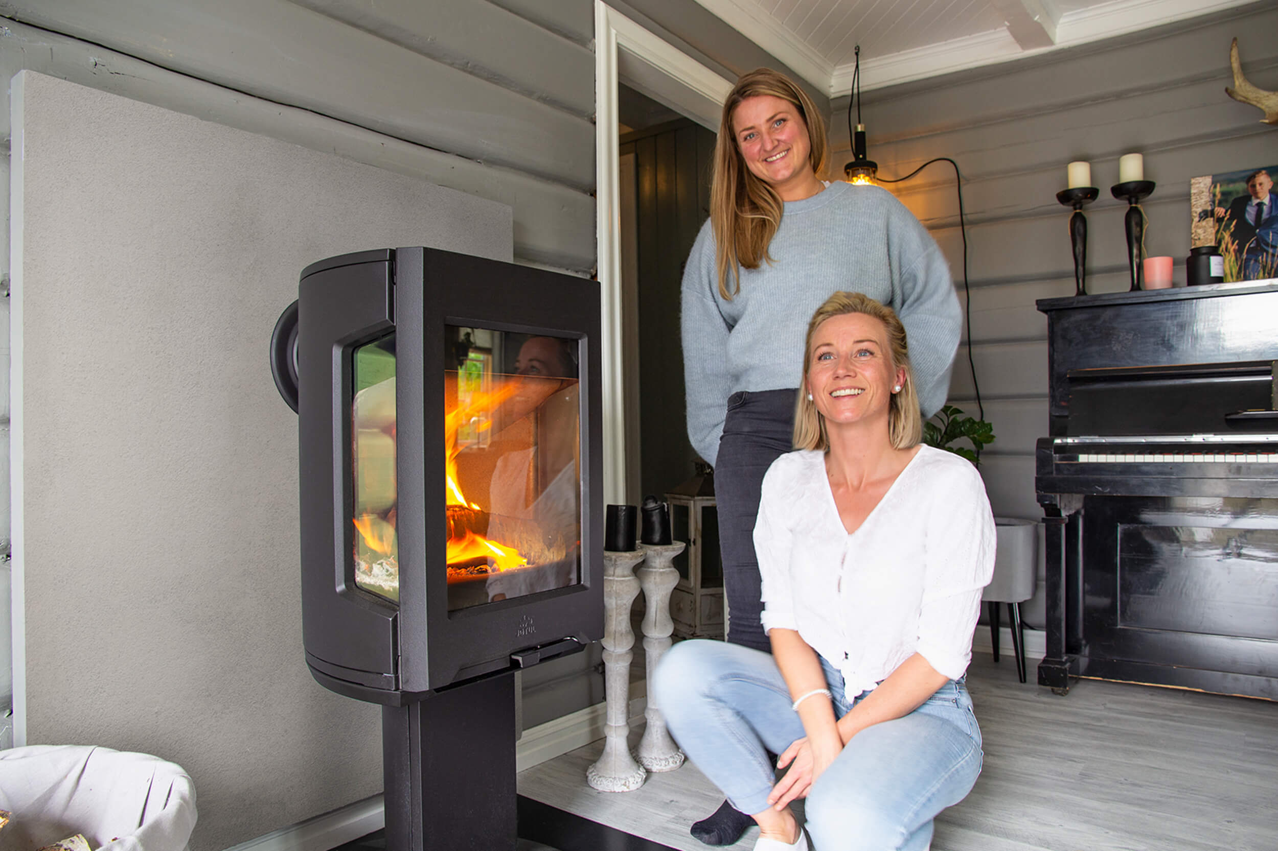 Jøtul vedovn med flammer i stue med to personer ved peisen med flammer